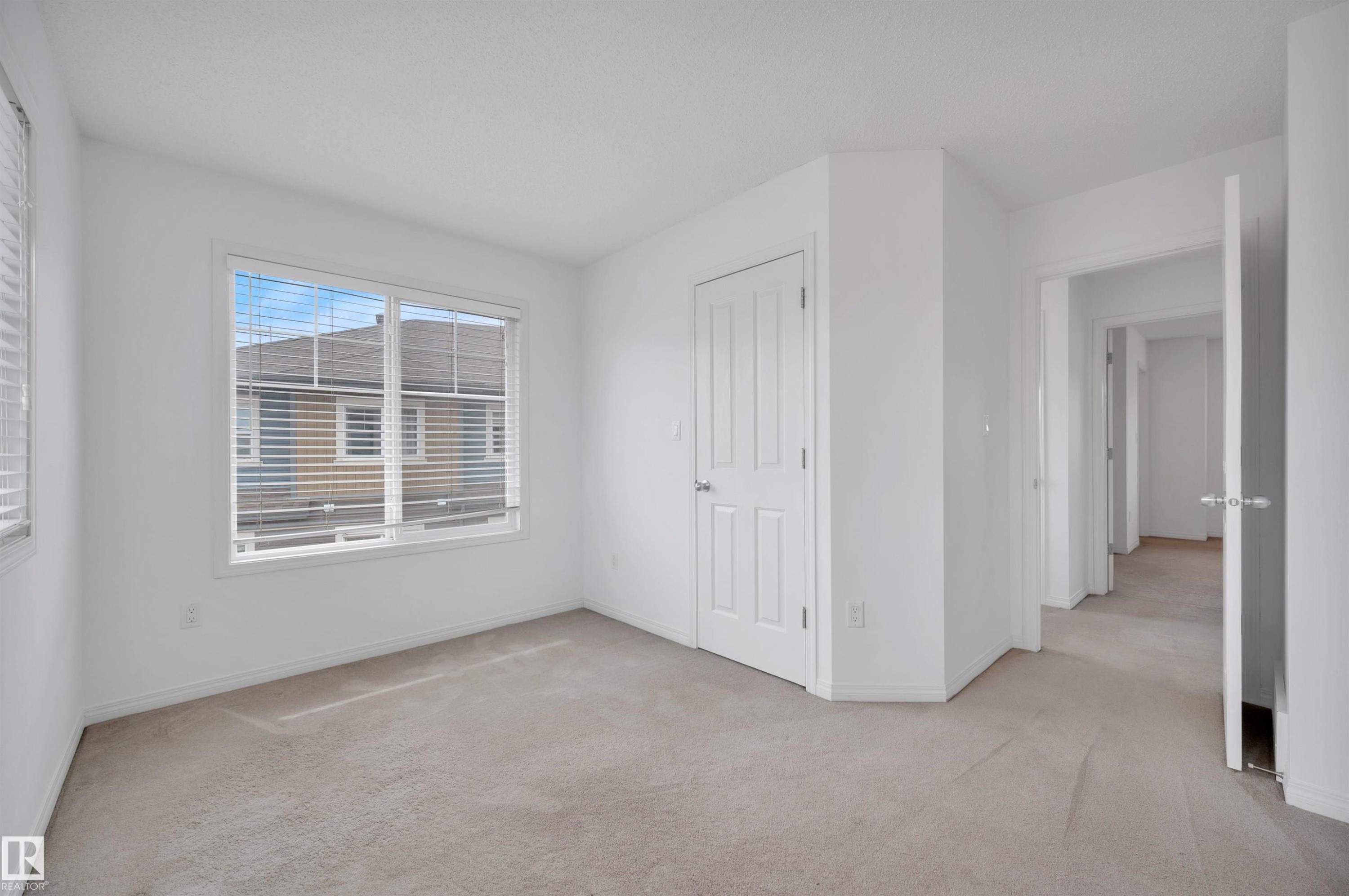 Bright room featuring two windows with blinds, light-colored carpeting, a paneled door, and neutral white wall finishes - 13 1030 Chappelle Boulevard, Edmonton, AB - Indoor Photo Showing Other Room