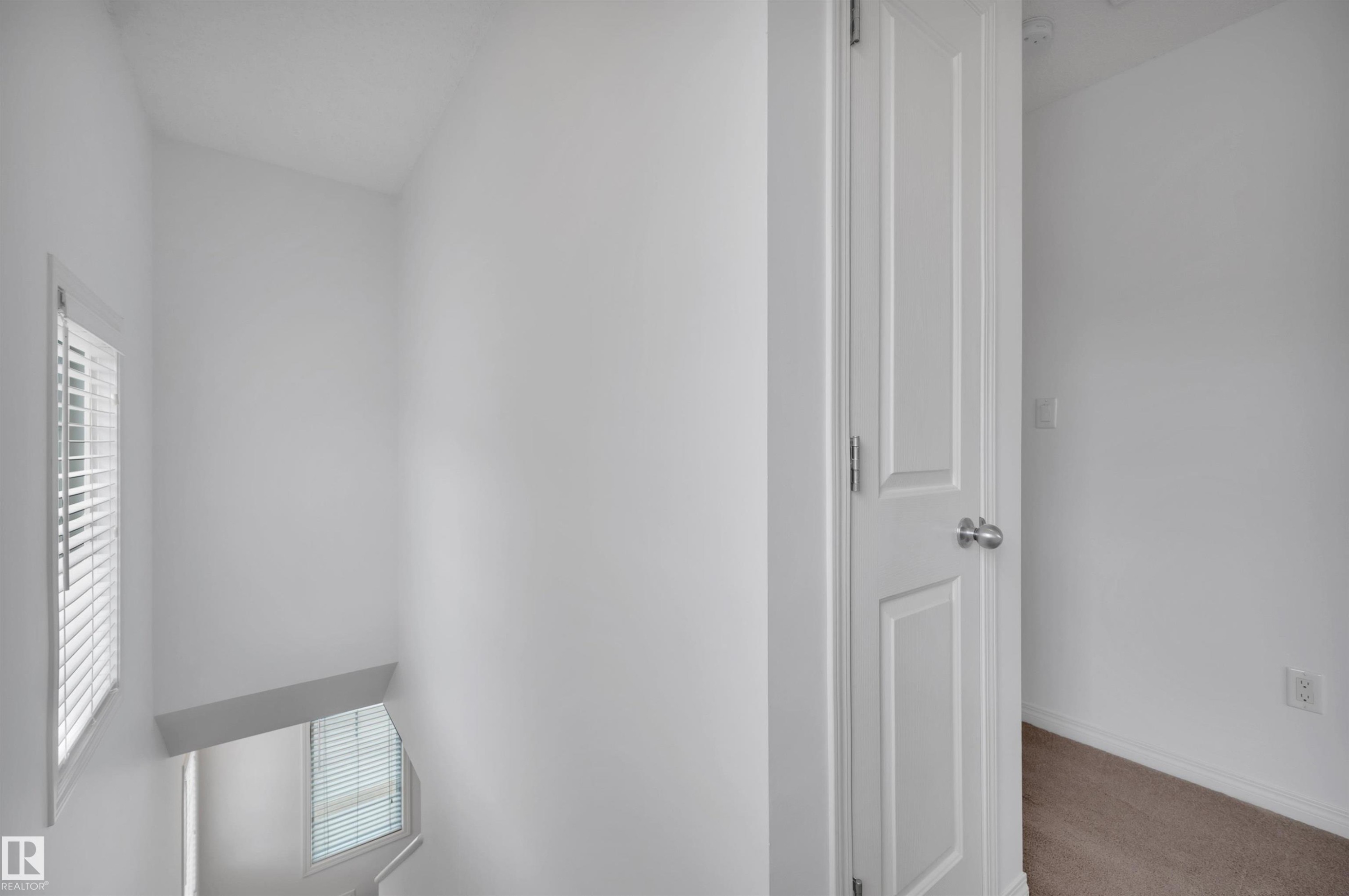 Staircase landing featuring white walls, a window with horizontal blinds, and a paneled interior door - 13 1030 Chappelle Boulevard, Edmonton, AB - Indoor Photo Showing Other Room