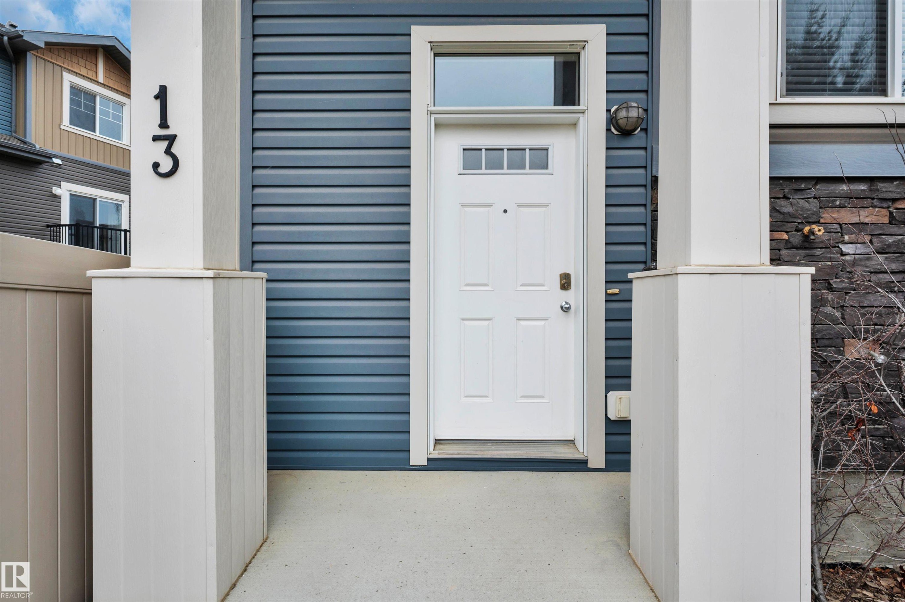 Front entry featuring a white paneled door with transom window, horizontal blue siding, architectural stone accents, and exterior lighting - 13 1030 Chappelle Boulevard, Edmonton, AB - Outdoor With Exterior