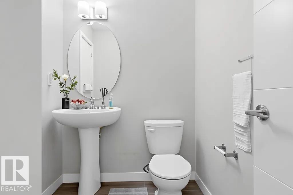 Bathroom featuring a white pedestal sink, oval mirror, and contemporary two-light vanity fixture - 18, 2560 Pegasus Boulevard, Edmonton, AB - Indoor Photo Showing Bathroom