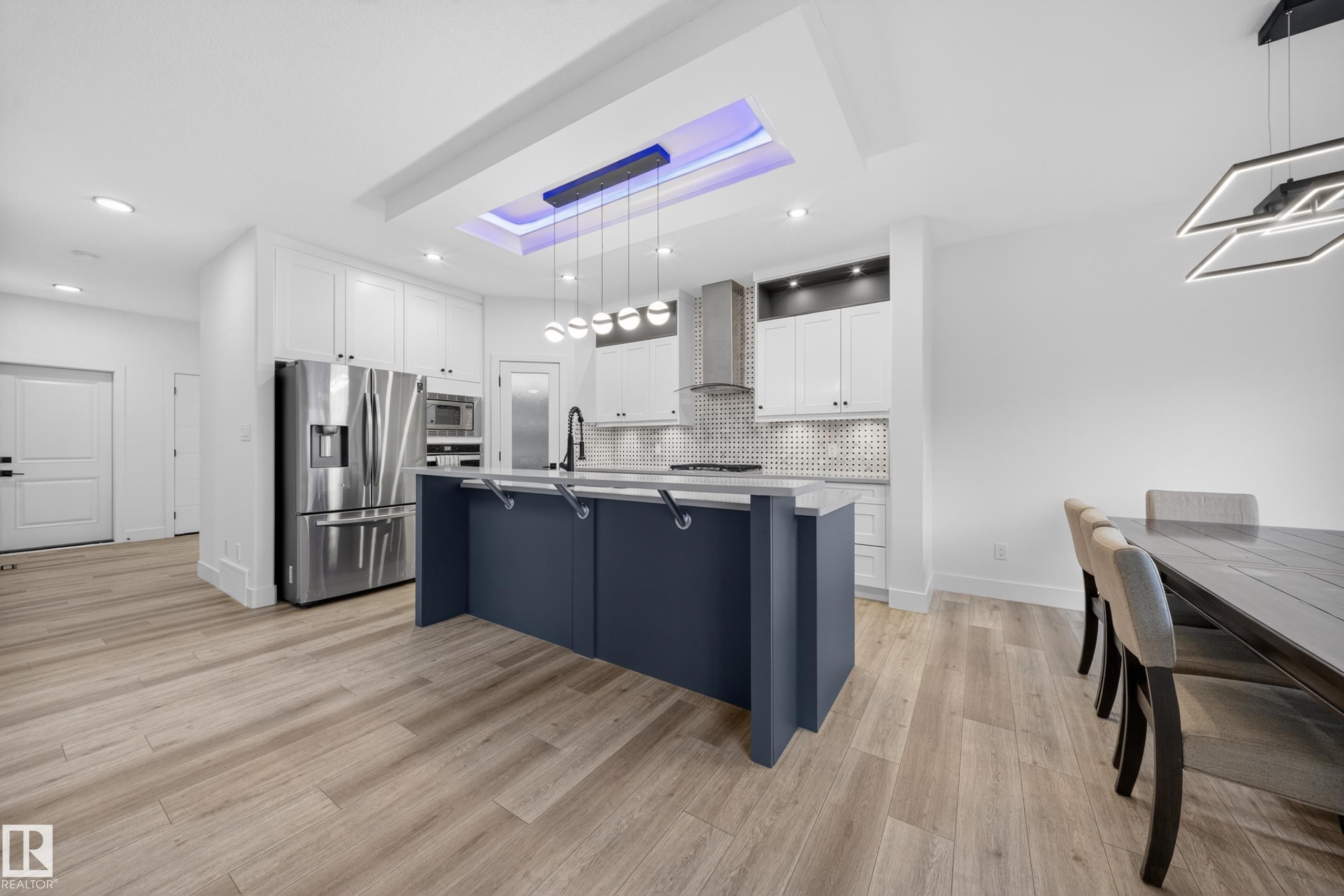 Contemporary kitchen featuring a large island with seating, stainless steel appliances, white cabinetry, and a decorative coffered ceiling detail with recessed lighting - 7414 Chivers Crescent Sw, Edmonton, AB - Indoor Photo Showing Kitchen With Upgraded Kitchen