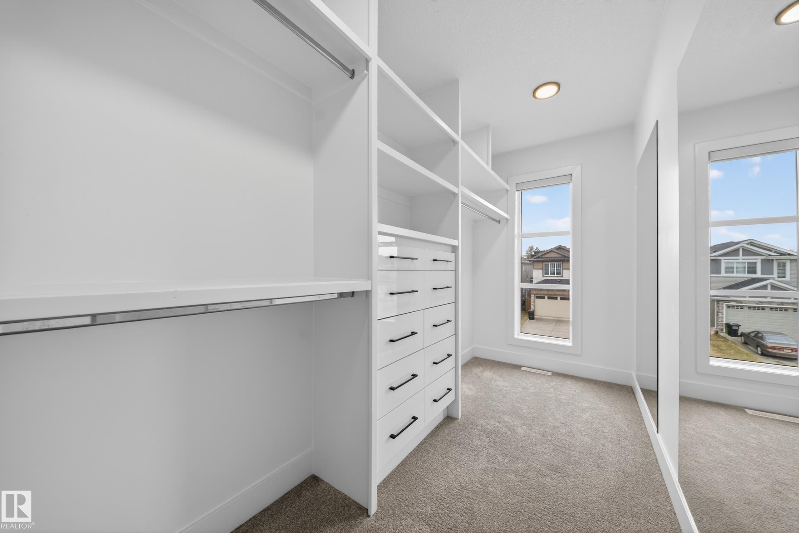 Custom white closet system featuring shelving, hanging rods, and built-in drawers with matte black hardware - 7414 Chivers Crescent Sw, Edmonton, AB - Indoor With Storage