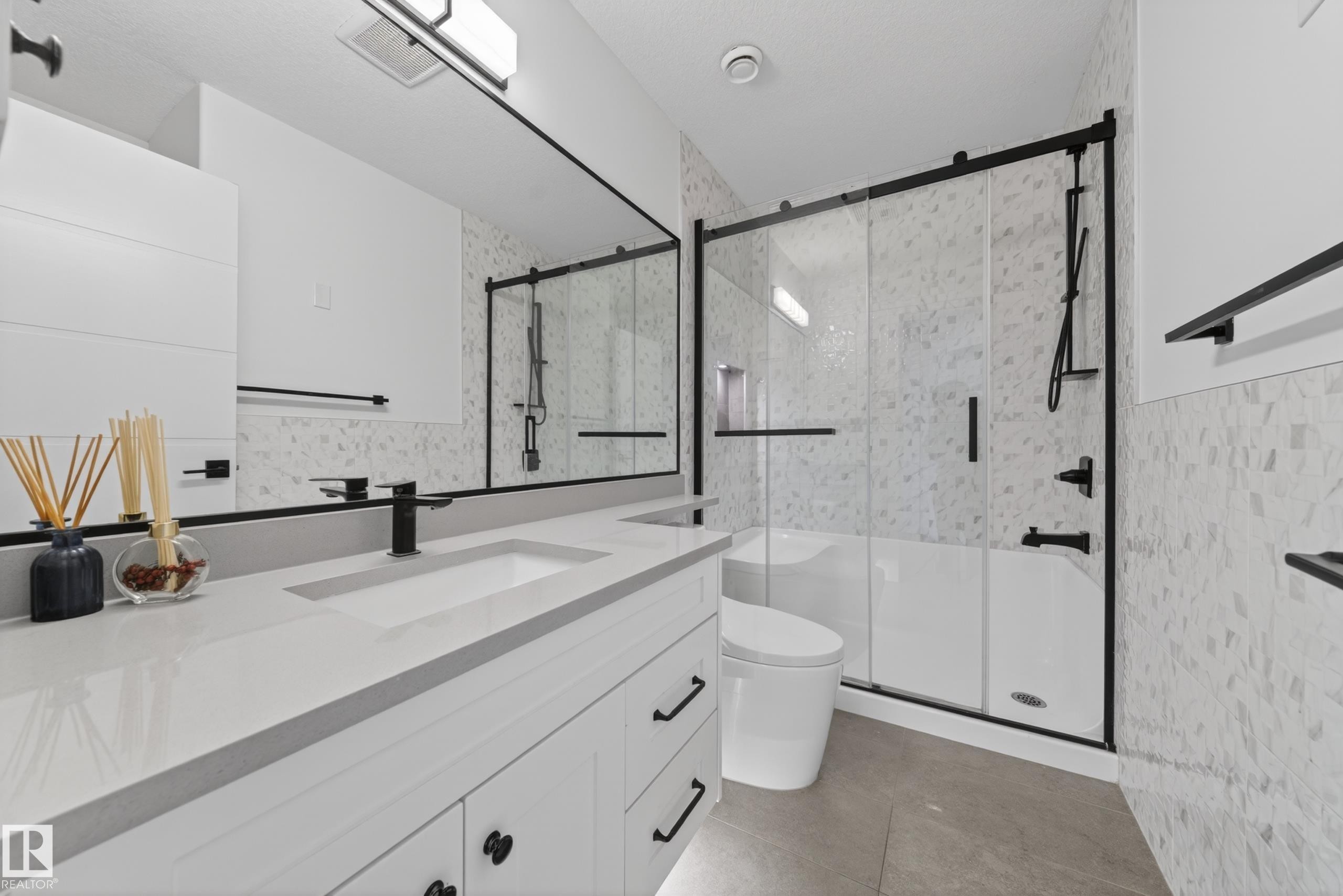 Contemporary bathroom featuring a spacious vanity with an integrated sink and light grey countertop, matte black fixtures, a large frameless mirror, and a shower-tub combination with sliding glass doors - 7414 Chivers Crescent Sw, Edmonton, AB - Indoor Photo Showing Bathroom