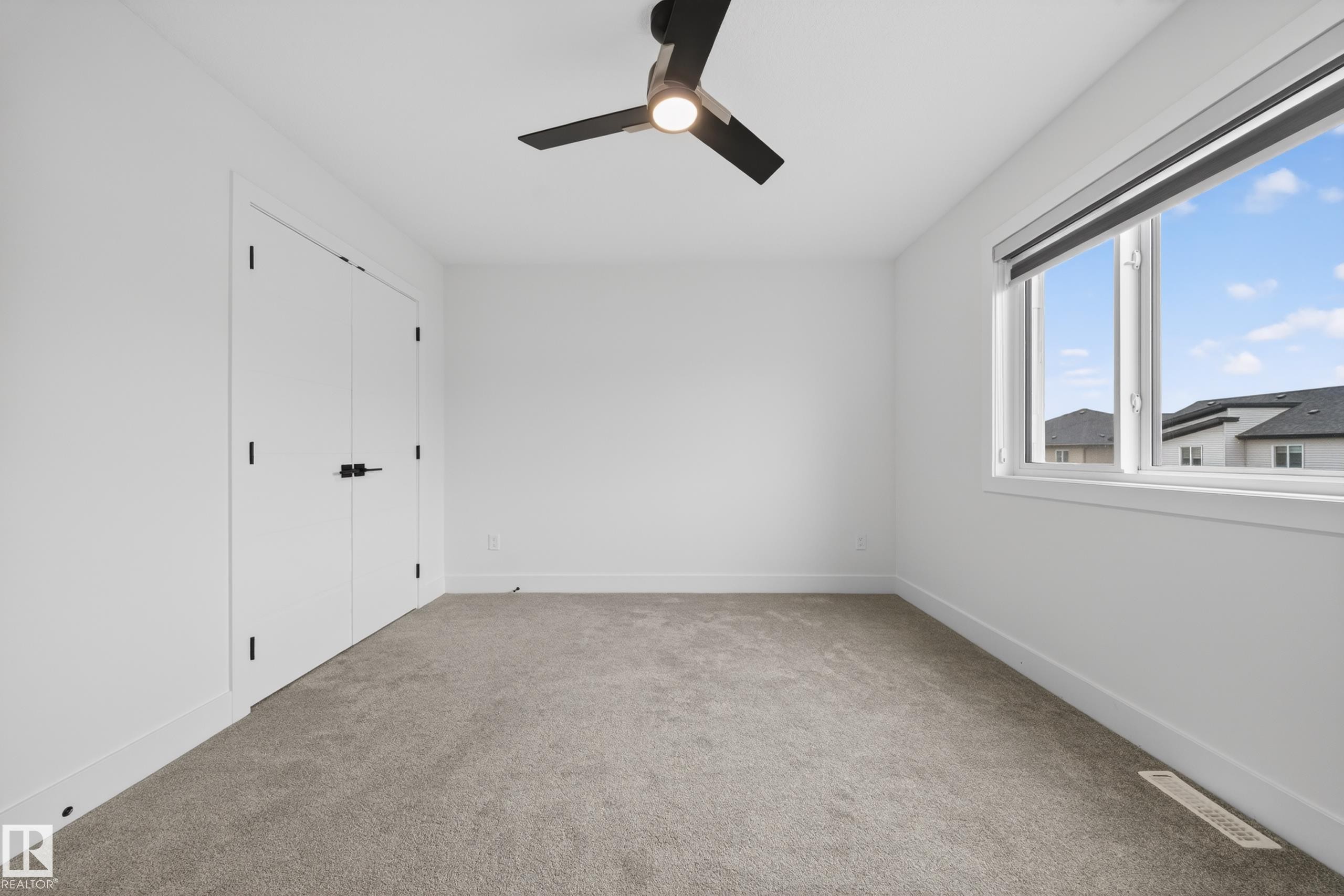 Bright room featuring a large window with roller shade, neutral carpeting, and a ceiling fan with integrated lighting - 7414 Chivers Crescent Sw, Edmonton, AB - Indoor Photo Showing Other Room
