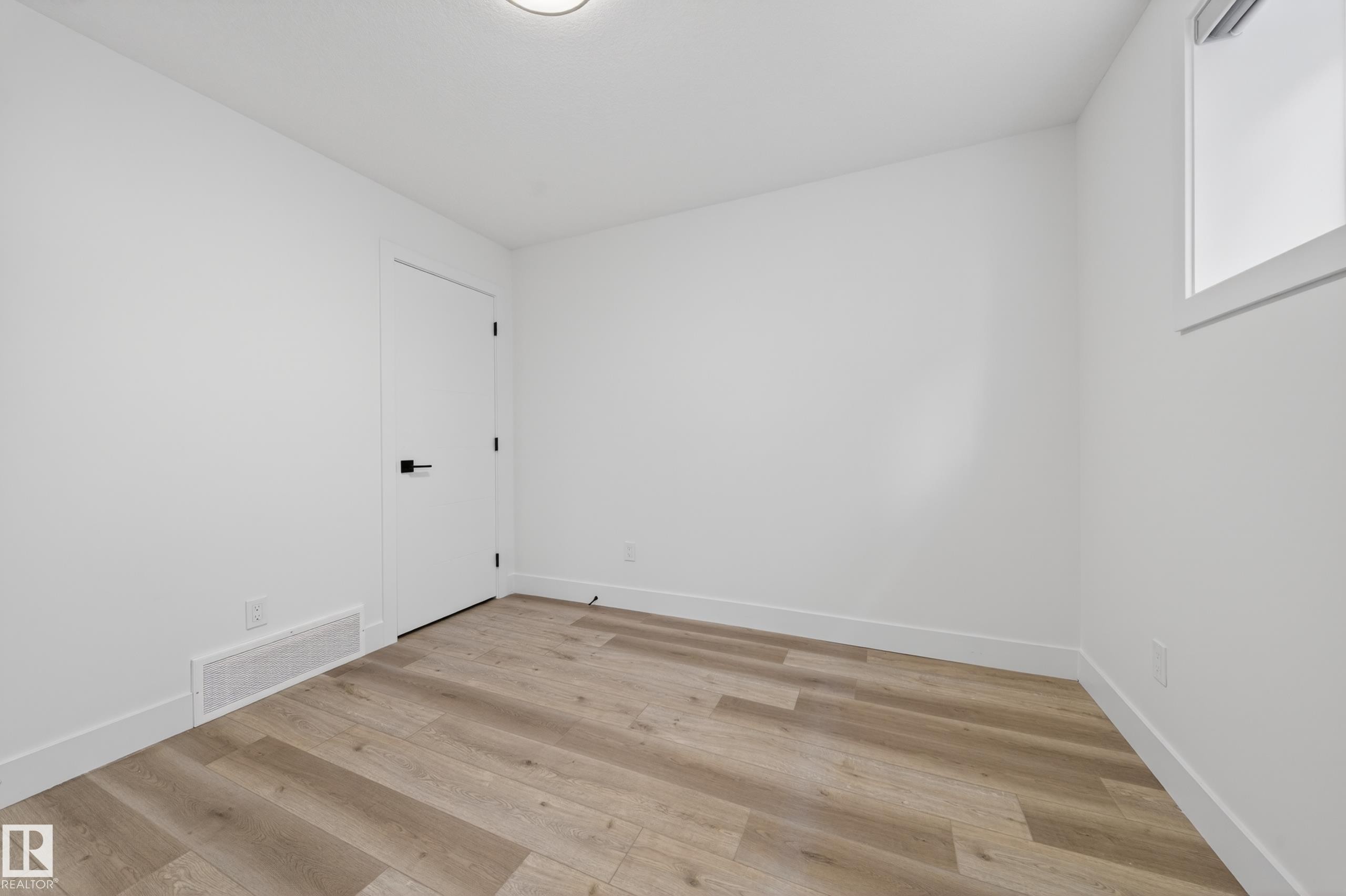 Room featuring wood-finish flooring, white walls, white trim, a white door with black hardware, and a single window - 7414 Chivers Crescent Sw, Edmonton, AB - Indoor Photo Showing Other Room