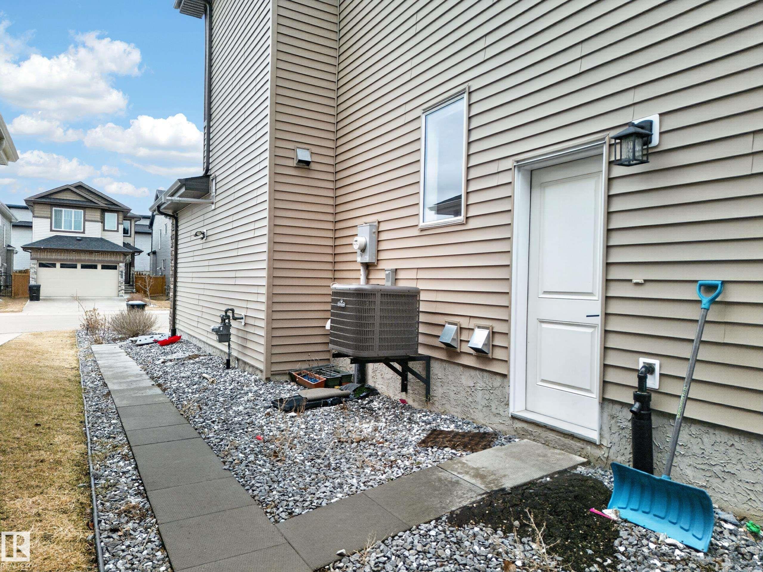 Tan horizontal siding exterior featuring a side entry door, exterior wall lantern, and a concrete paver walkway - 7414 Chivers Crescent Sw, Edmonton, AB - Outdoor