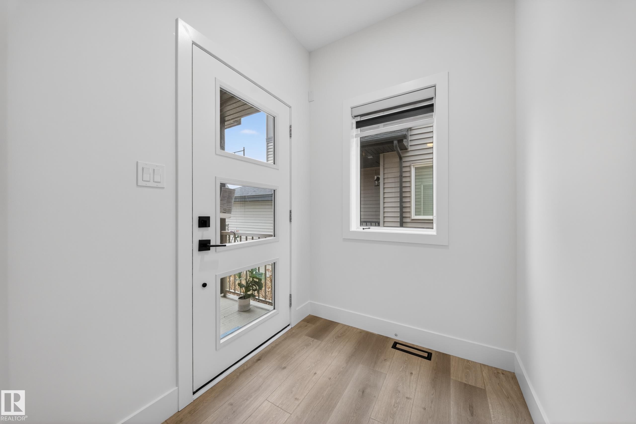 Entryway featuring a white door with three vertical glass panels, black hardware, and wood-finish flooring - 7414 Chivers Crescent Sw, Edmonton, AB - Indoor Photo Showing Other Room