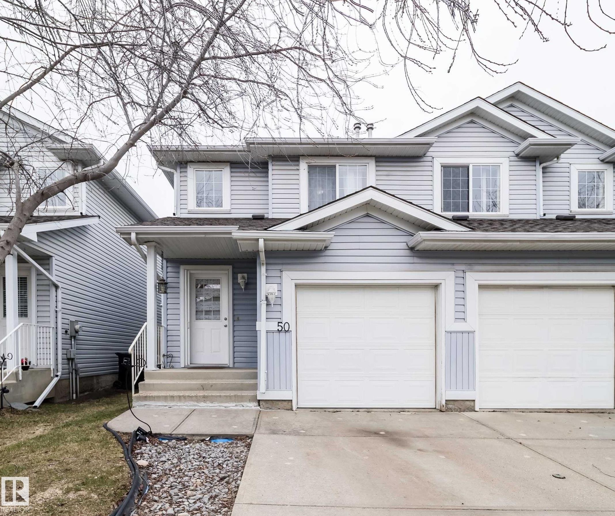 Two-story residence featuring light blue siding, a double garage with white doors, and a concrete driveway - 50 14603 Miller Boulevard, Edmonton, AB