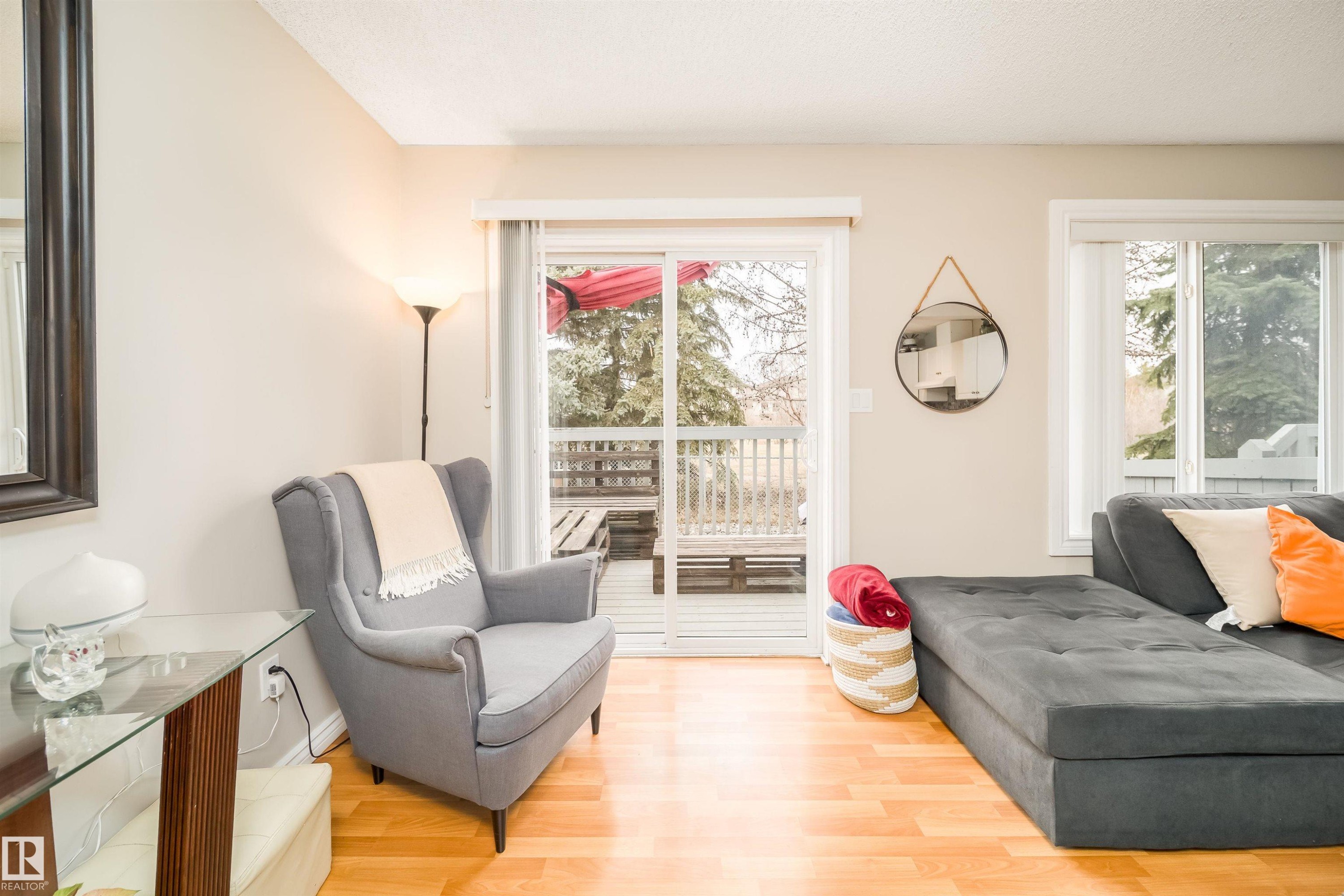 Living area featuring wood-finish flooring, light-toned walls, and a sliding glass door providing exterior access to a wood-decked outdoor space - 50 14603 Miller Boulevard, Edmonton, AB