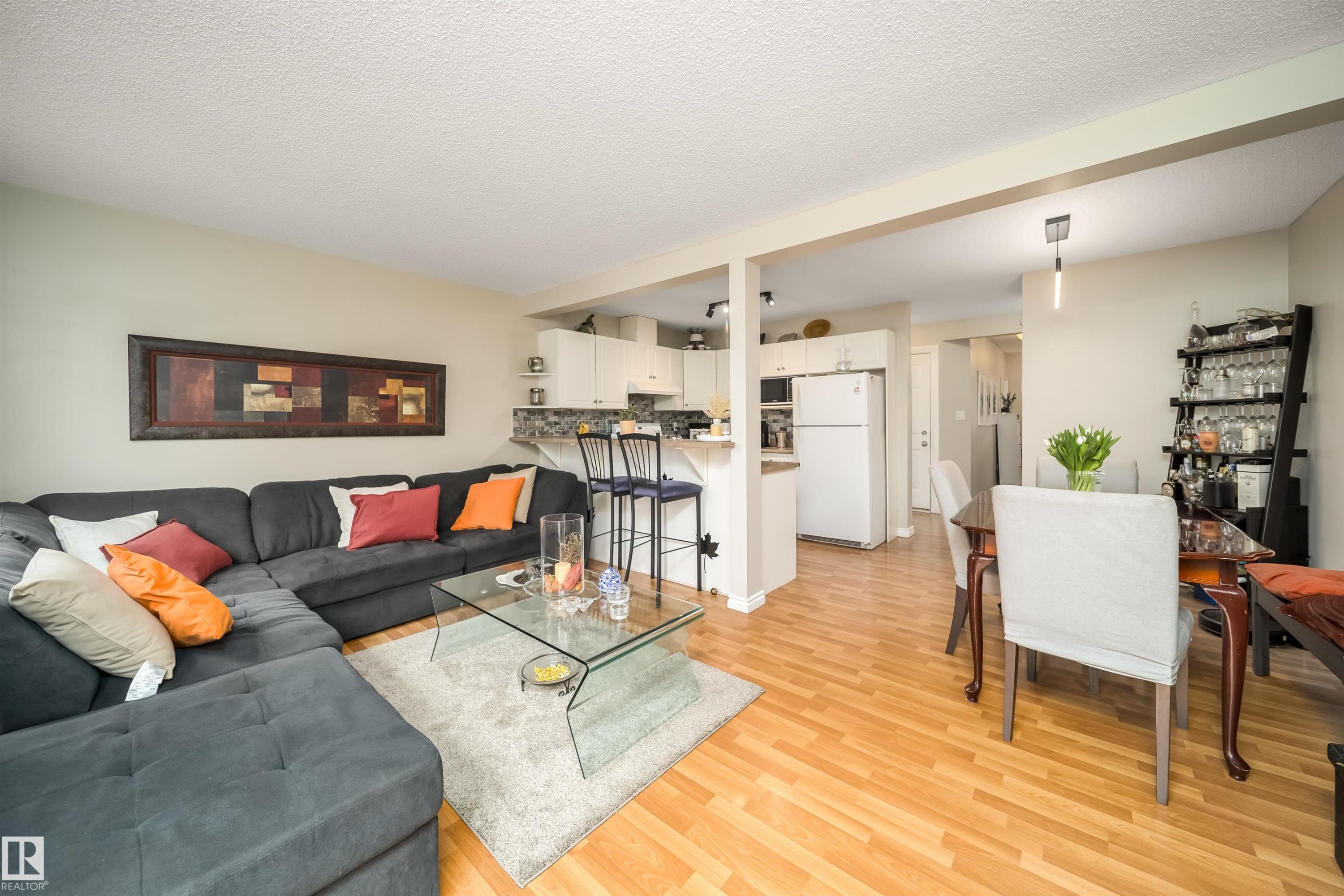 Open-concept living space featuring wood-finish flooring, a kitchen with white cabinetry and a breakfast bar, and a dining area with pendant lighting - 50 14603 Miller Boulevard, Edmonton, AB