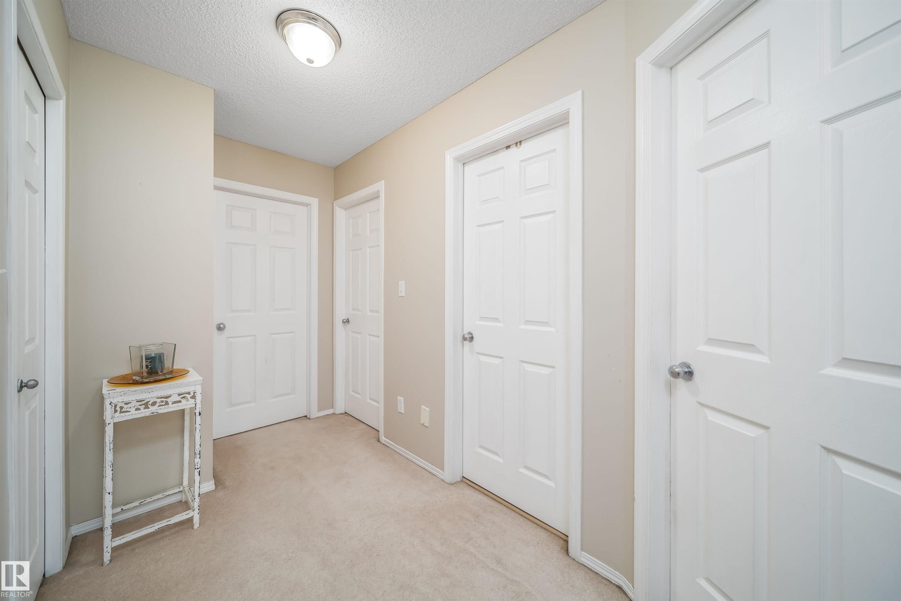 Hallway featuring neutral-toned walls, light-colored carpeting, white panel doors, and a flush-mount ceiling light fixture - 50 14603 Miller Boulevard, Edmonton, AB