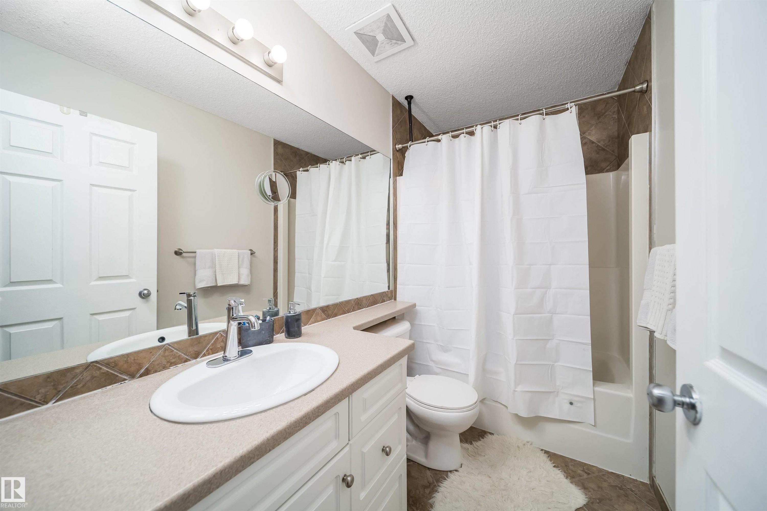 Bathroom featuring a white vanity with a light-toned countertop, an oval undermount sink, and chrome fixtures - 50 14603 Miller Boulevard, Edmonton, AB