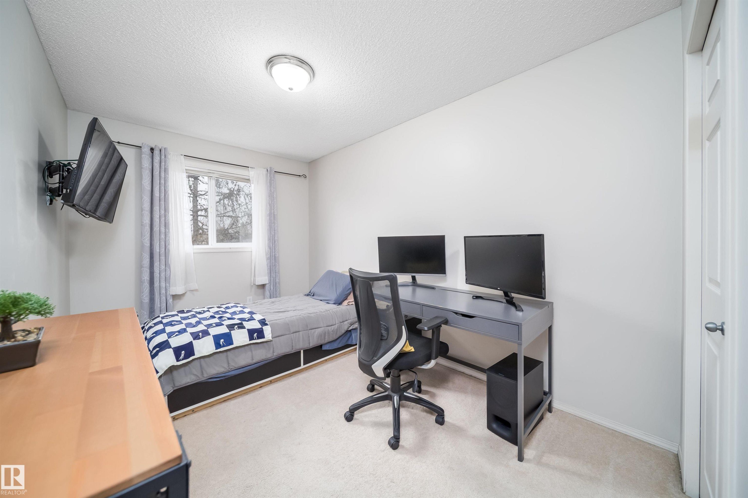 Carpeted room featuring a white paneled door, flush-mount ceiling light, and a window with sheer and patterned curtains - 50 14603 Miller Boulevard, Edmonton, AB
