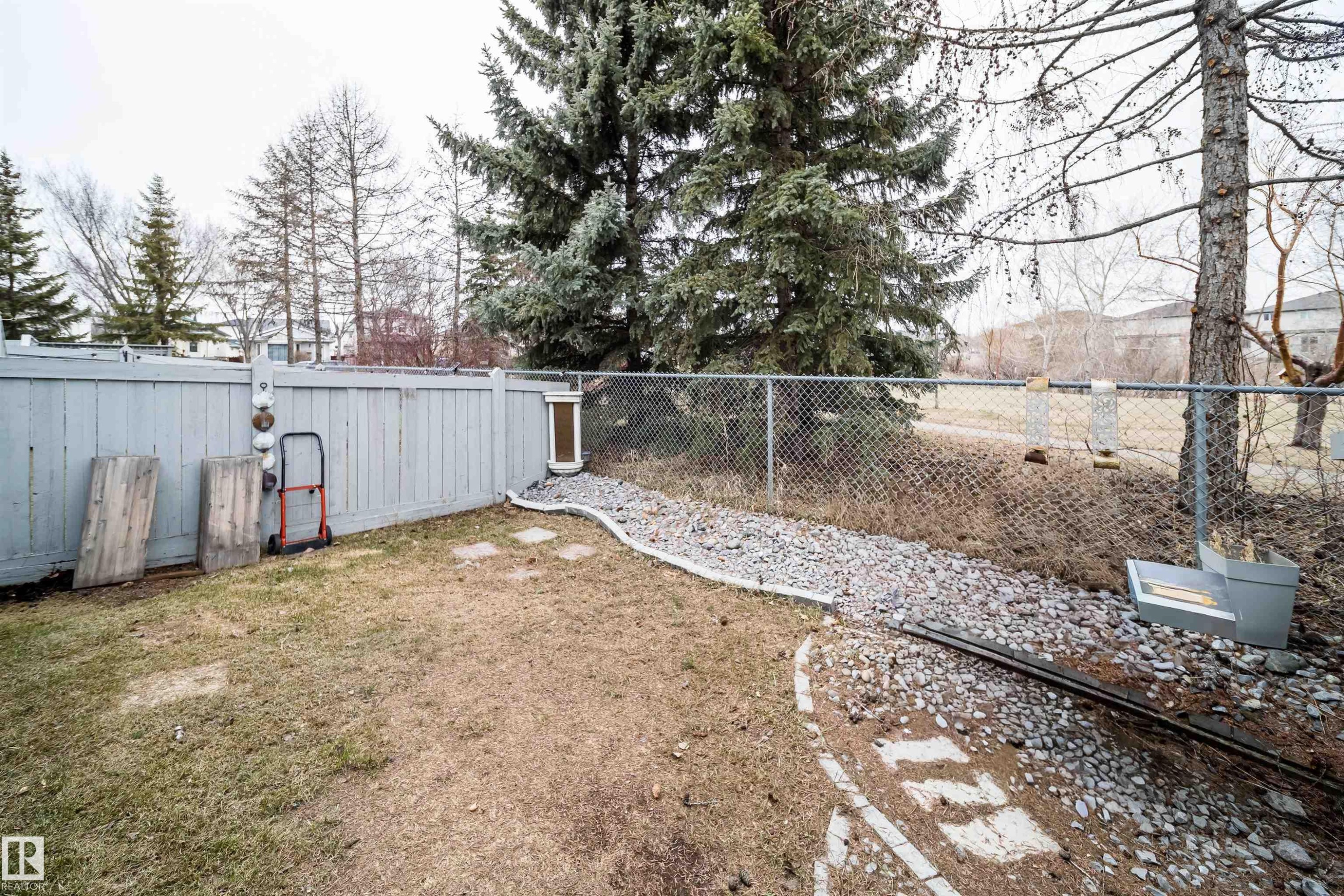 Fenced backyard featuring a gravel bed and mature evergreen trees - 50 14603 Miller Boulevard, Edmonton, AB