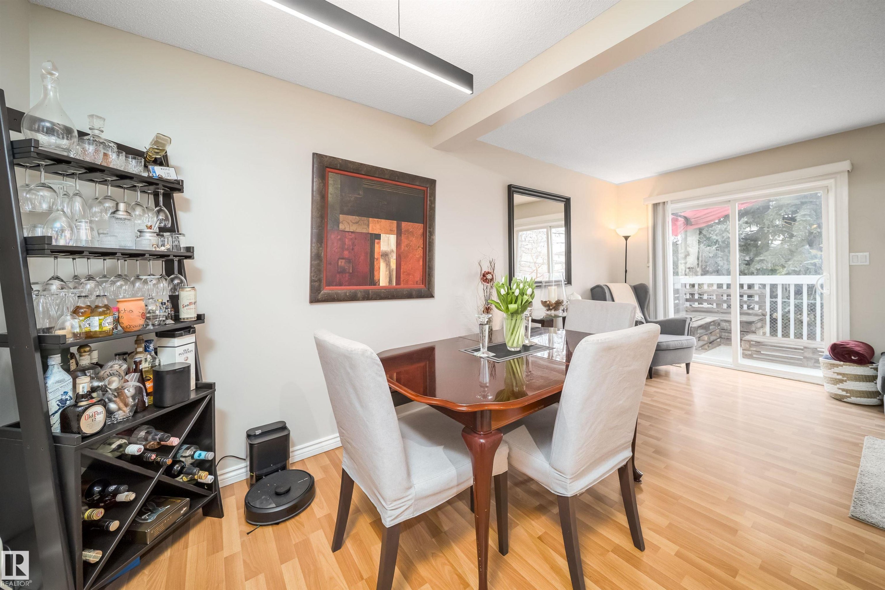 Open-concept living area featuring light wood-finish flooring, a contemporary linear overhead light fixture, a glass sliding door providing access to an exterior space, and light neutral wall tones - 50 14603 Miller Boulevard, Edmonton, AB