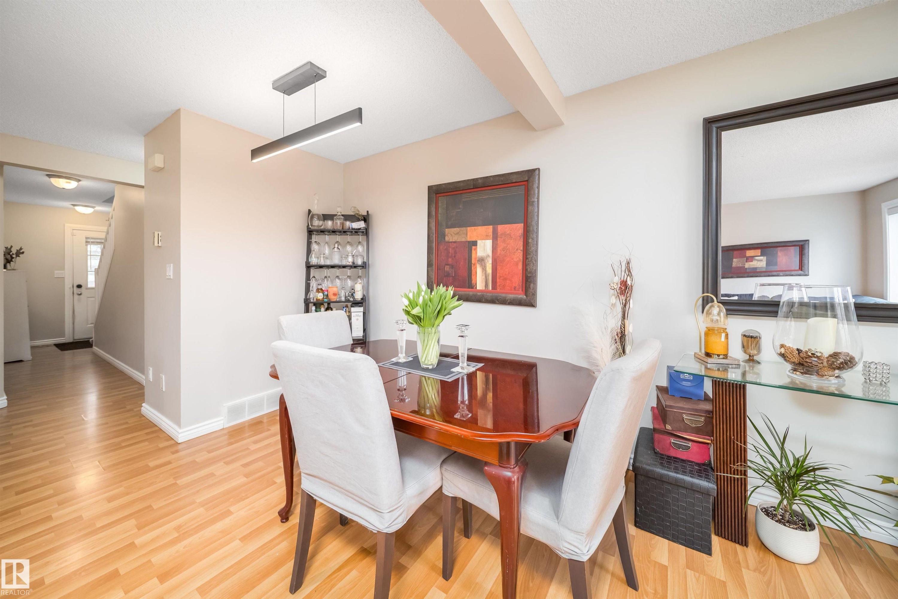 Dining area featuring wood-finish flooring, a contemporary linear pendant light fixture, and a built-in shelving unit - 50 14603 Miller Boulevard, Edmonton, AB