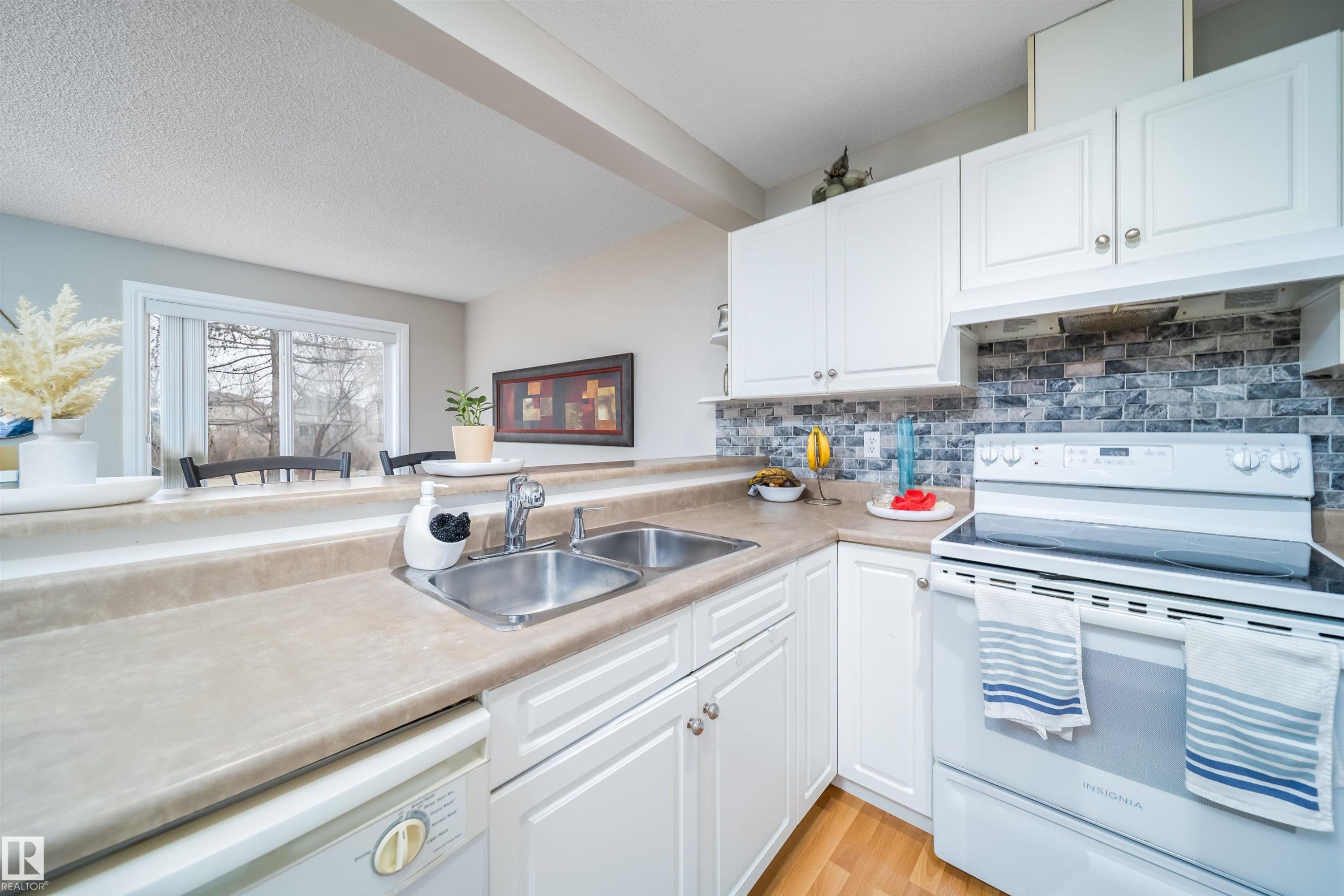 Kitchen featuring white cabinetry, a dual basin stainless steel sink, and a light-toned countertop - 50 14603 Miller Boulevard, Edmonton, AB