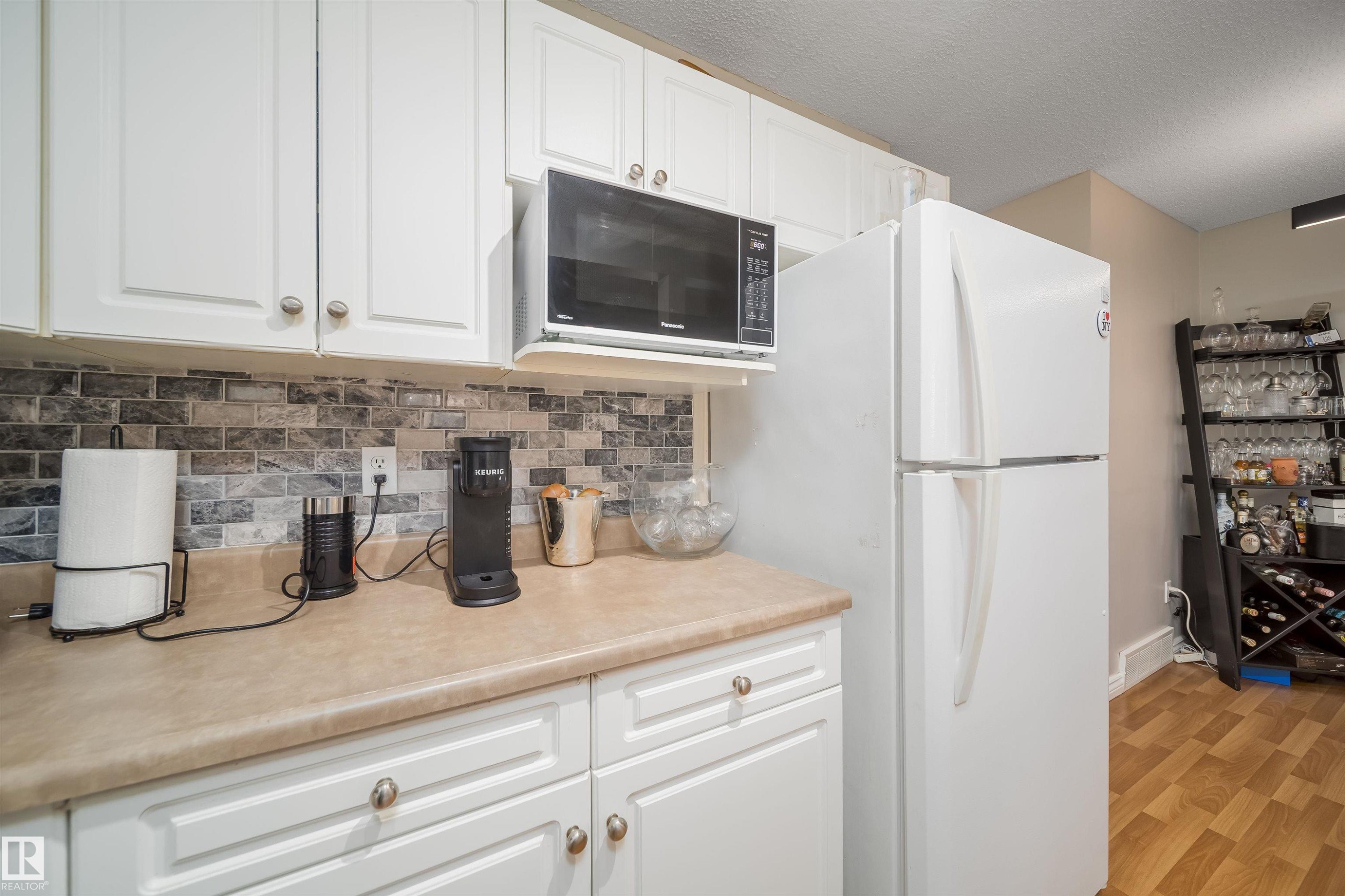 Kitchen featuring white cabinetry, light-toned countertops, and a mosaic tile backsplash - 50 14603 Miller Boulevard, Edmonton, AB