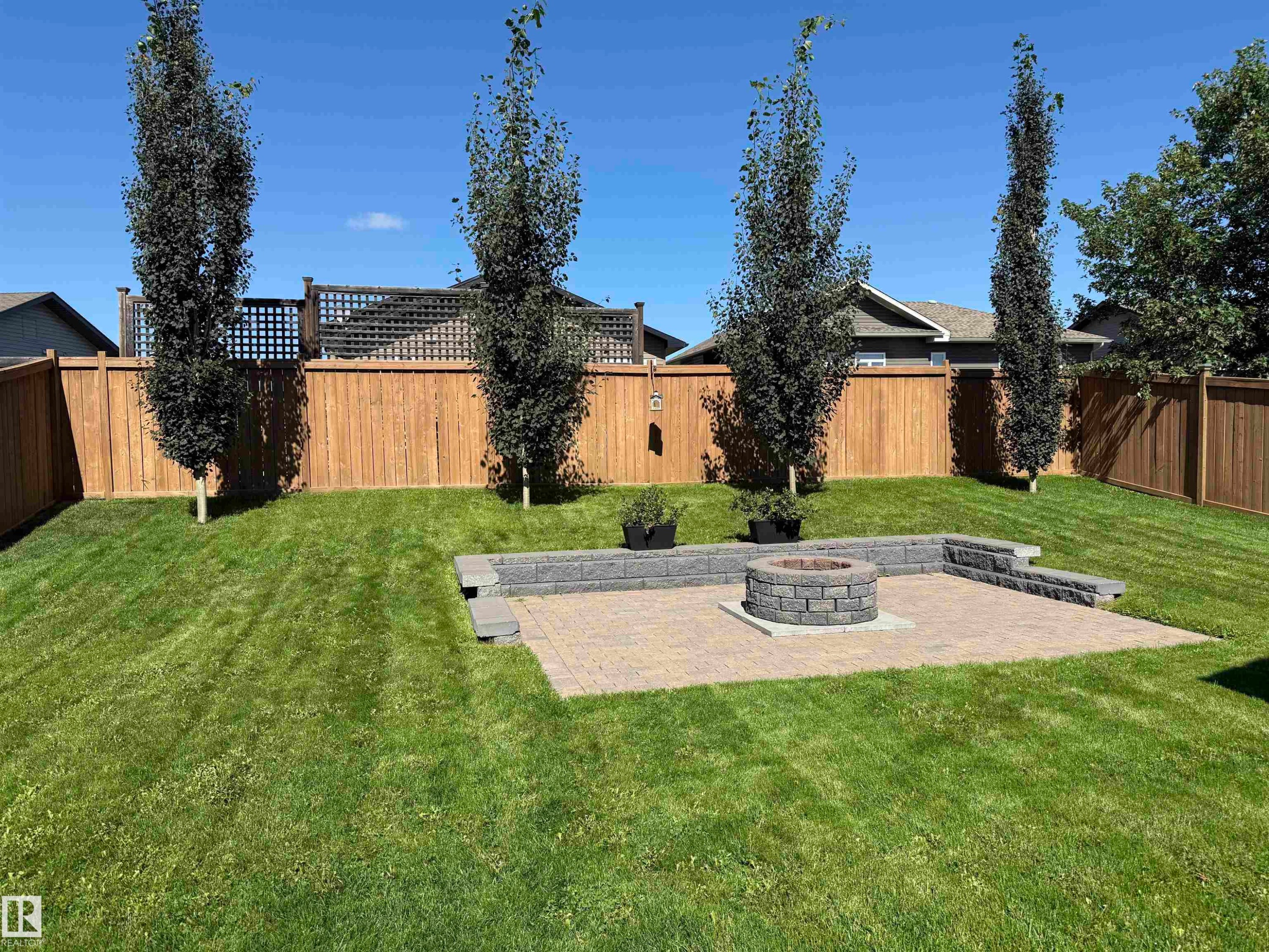 Expansive backyard featuring a paver patio with a built-in fire pit, surrounded by lush green lawn - 4926 58 Ave, Cold Lake, AB - Outdoor