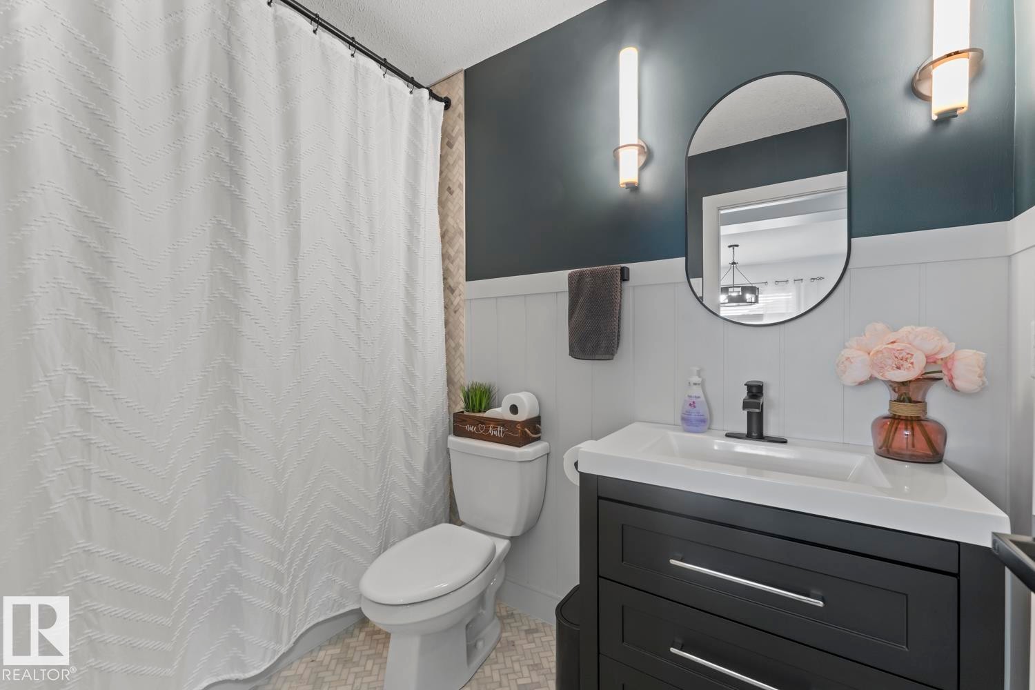 Contemporary bathroom featuring a dark vanity with a white countertop, oval wall-mounted mirror, and black fixtures - 4926 58 Ave, Cold Lake, AB - Indoor Photo Showing Bathroom