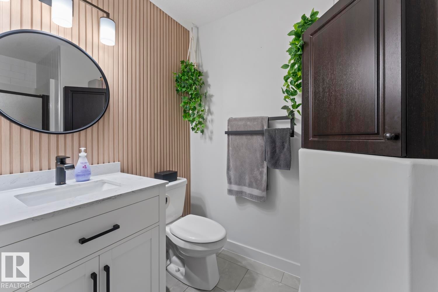 Modern bathroom featuring a white vanity with an integrated sink and matte black hardware, a black-framed circular mirror, and a linear light fixture - 4926 58 Ave, Cold Lake, AB - Indoor Photo Showing Bathroom