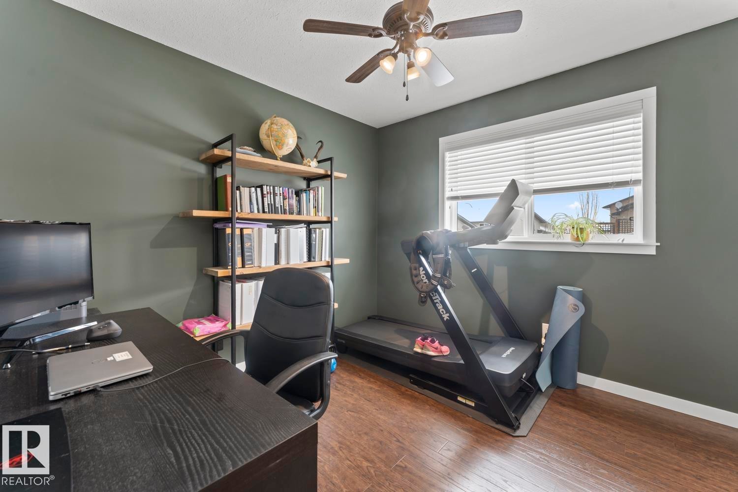 Room featuring wood-finish flooring, a ceiling fan with integrated lighting, a window with horizontal blinds, and dark-toned walls - 4926 58 Ave, Cold Lake, AB - Indoor Photo Showing Office