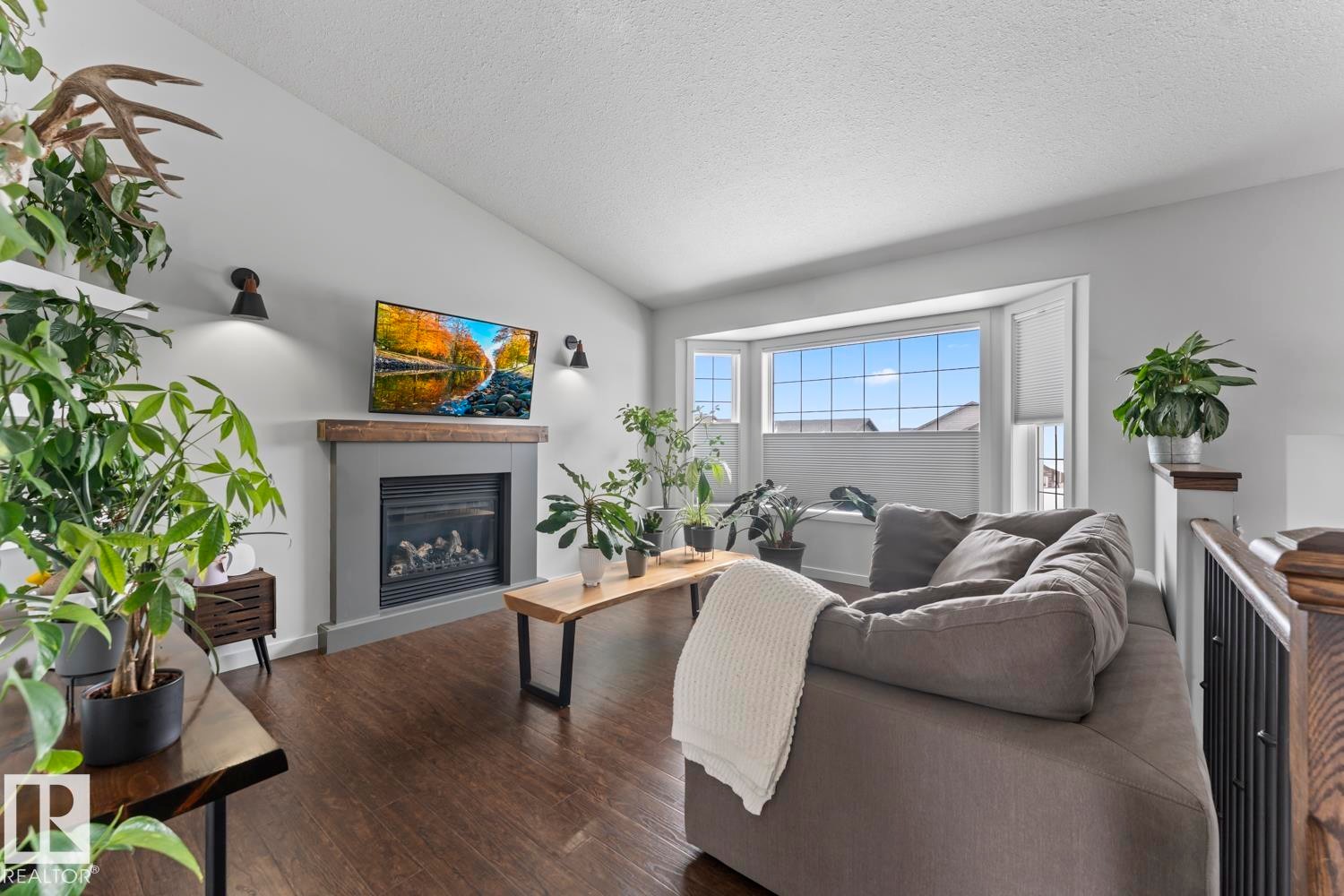 Living area featuring a gas fireplace with a wood mantle, vaulted ceiling, wood-finish flooring, and a large bay window - 4926 58 Ave, Cold Lake, AB - Indoor Photo Showing Living Room With Fireplace