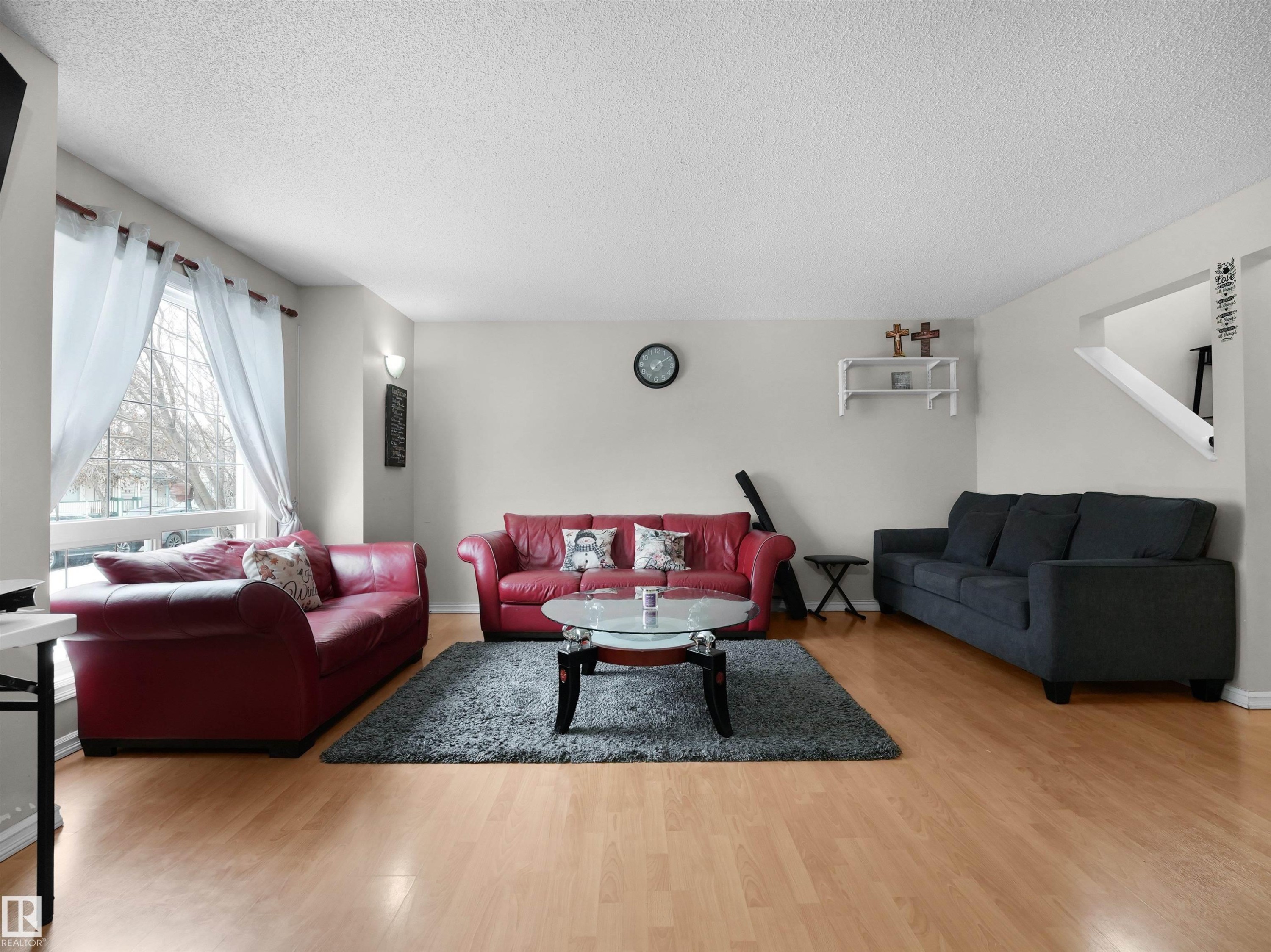 Bright open-concept living area featuring light wood-finish flooring, a large picture window with white sheer curtains, and light neutral wall colors - 21379 89 Avenue Nw, Edmonton, AB - Indoor Photo Showing Living Room