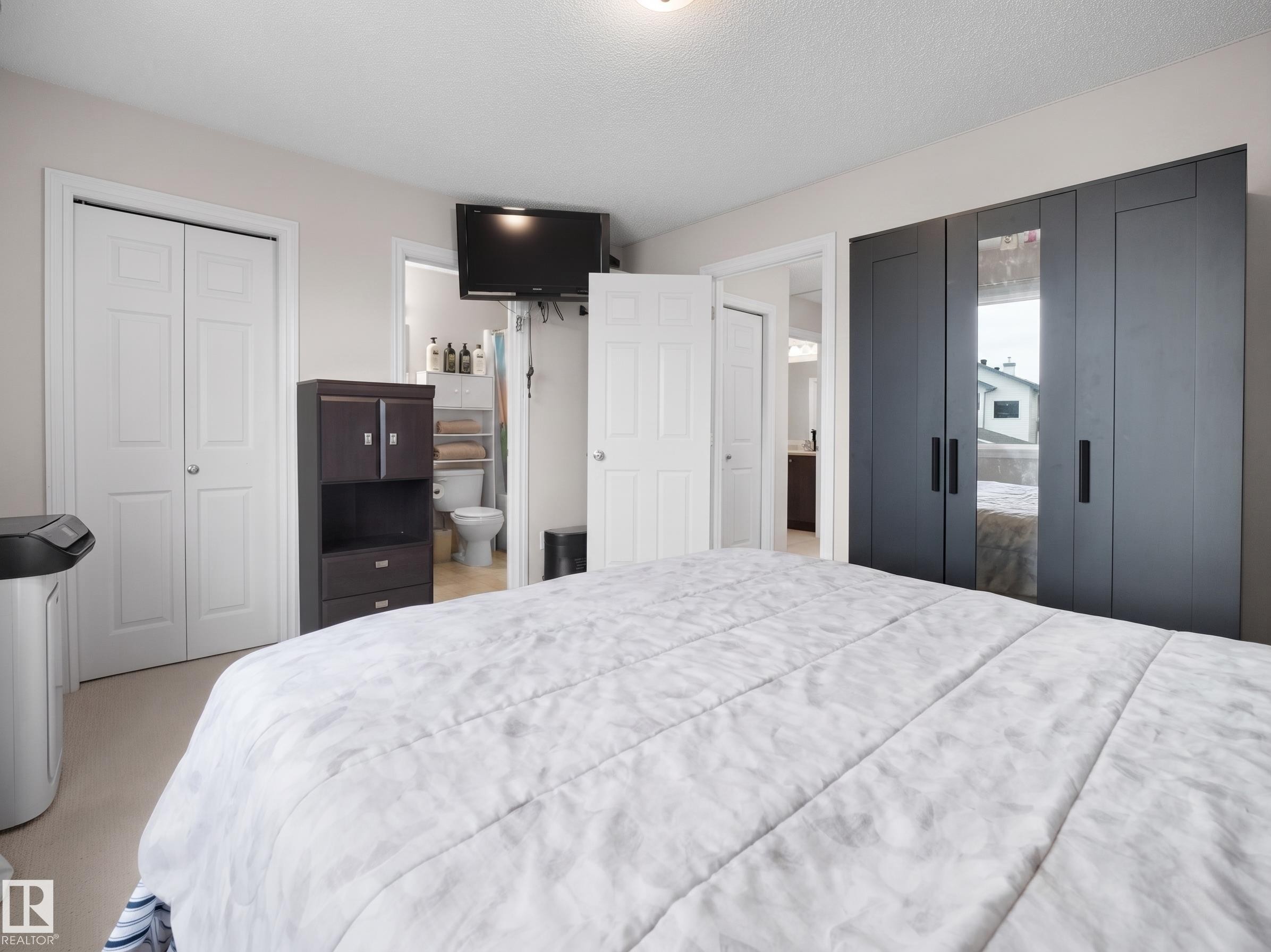 Bedroom featuring light-colored walls, carpet flooring, a dark-toned wardrobe with integrated mirrors, and white bi-fold closet doors - 21379 89 Avenue Nw, Edmonton, AB - Indoor Photo Showing Bedroom