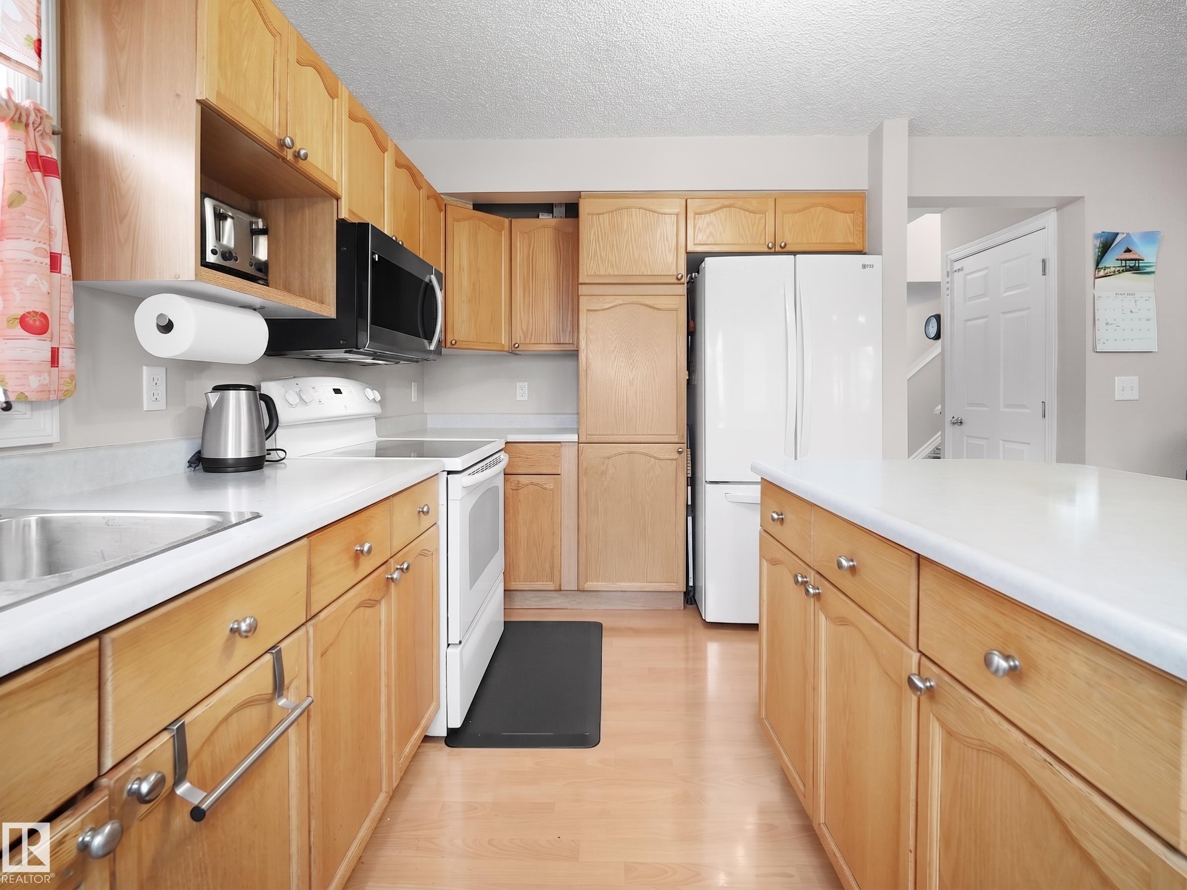 Light wood-finish cabinetry, white countertops, stainless steel sink, and wood-finish flooring define this kitchen space - 21379 89 Avenue Nw, Edmonton, AB - Indoor Photo Showing Kitchen