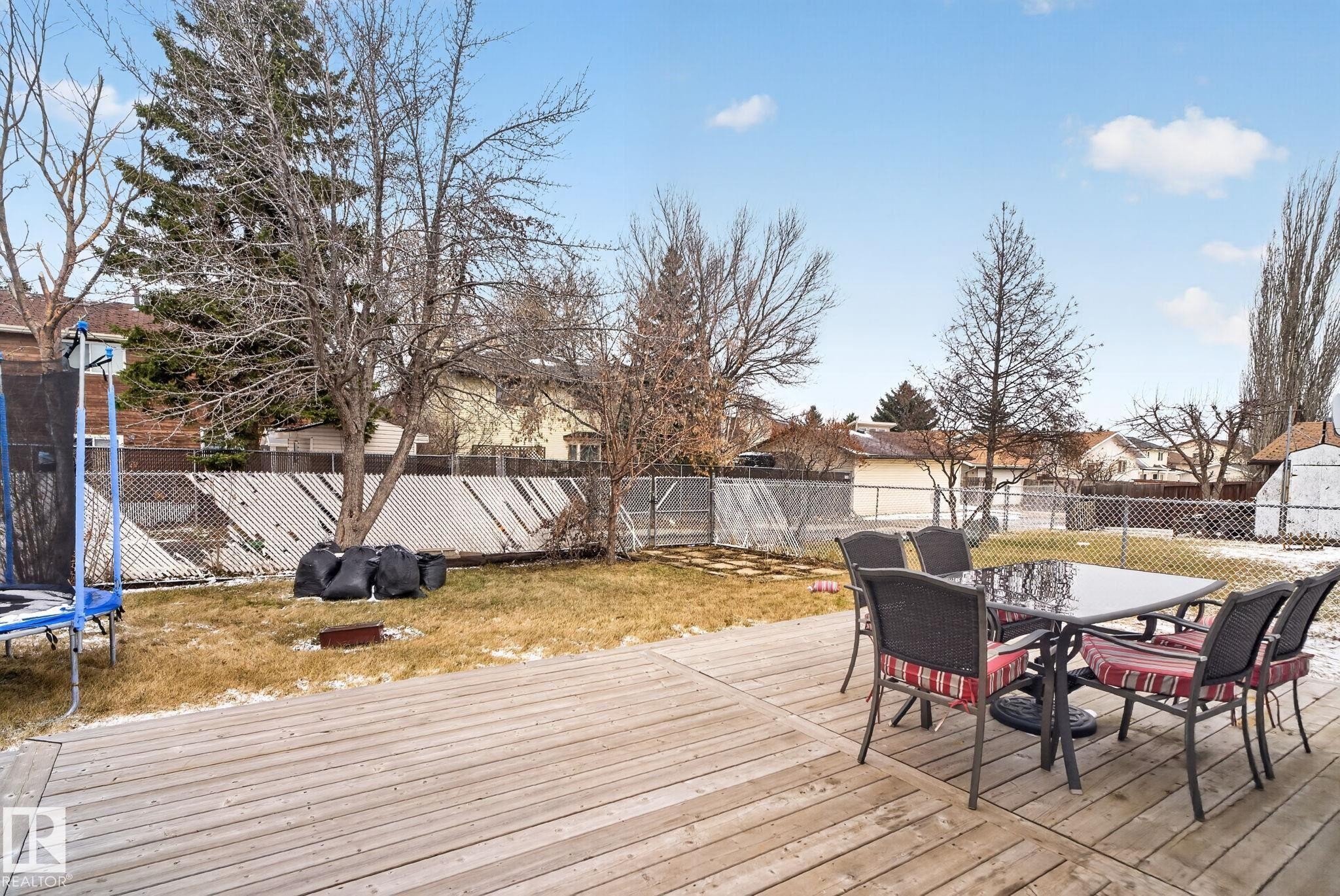 Expansive backyard featuring a wood deck, mature trees, chain-link fencing, and a storage shed - 18604 97A Avenue, Edmonton, AB - Outdoor With Deck Patio Veranda