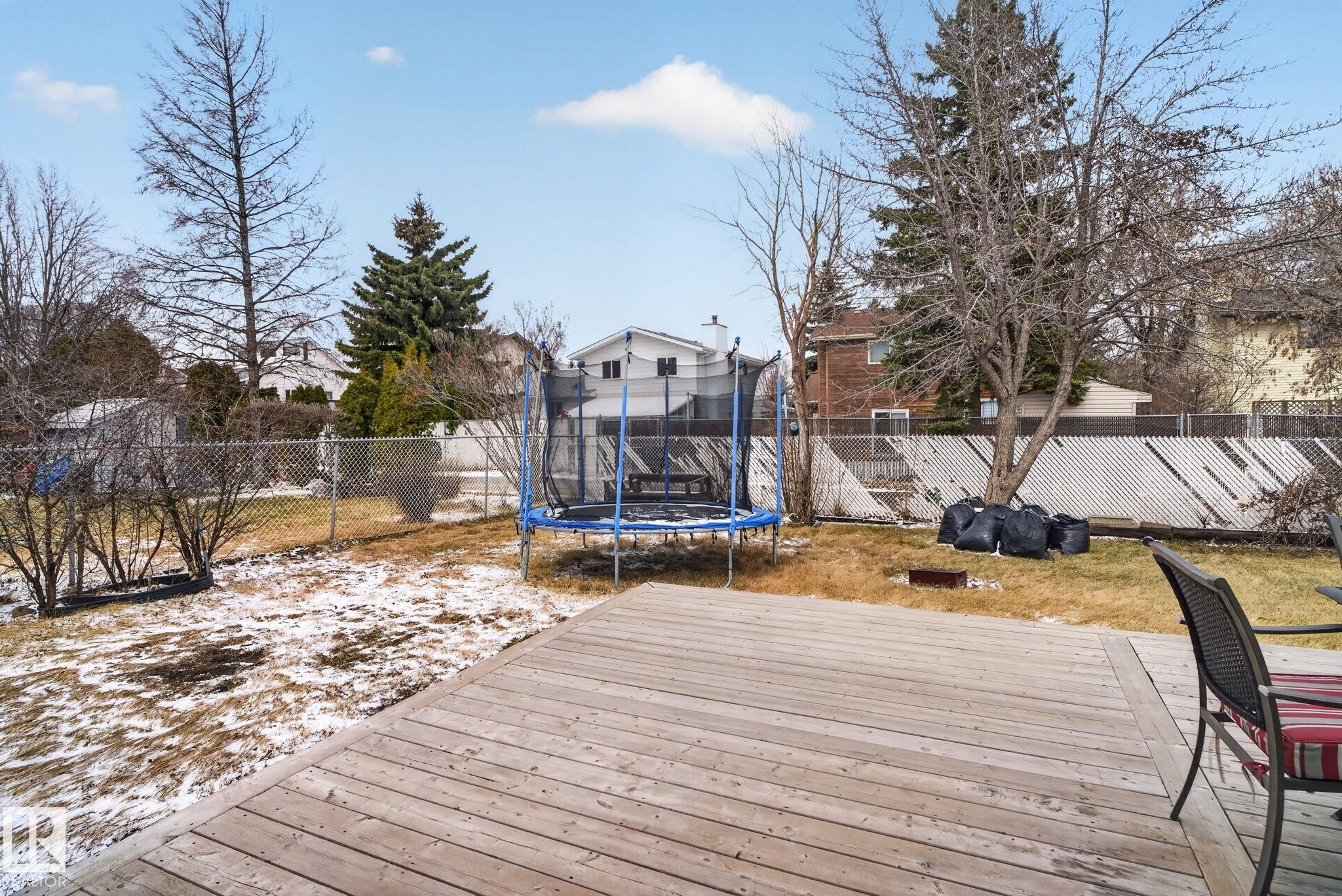 Expansive backyard featuring a large wooden deck, mature trees, and a chain-link fence - 18604 97A Avenue, Edmonton, AB - Outdoor With Deck Patio Veranda
