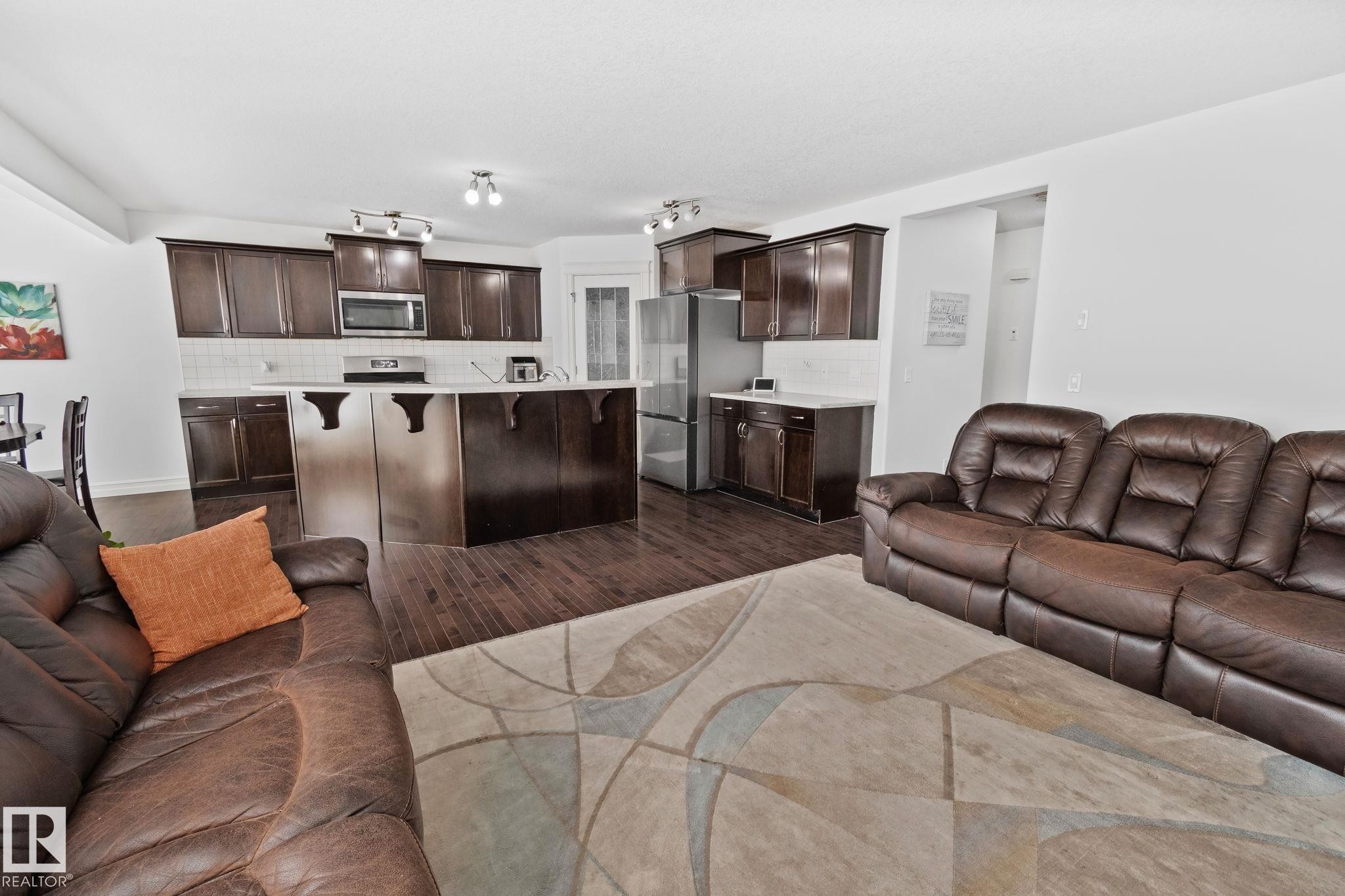 Spacious open concept living area featuring dark wood flooring, a kitchen with dark cabinetry, stainless steel appliances, and a central island, all illuminated by recessed lighting - 1115 61 Street, Edmonton, AB - Indoor Photo Showing Living Room