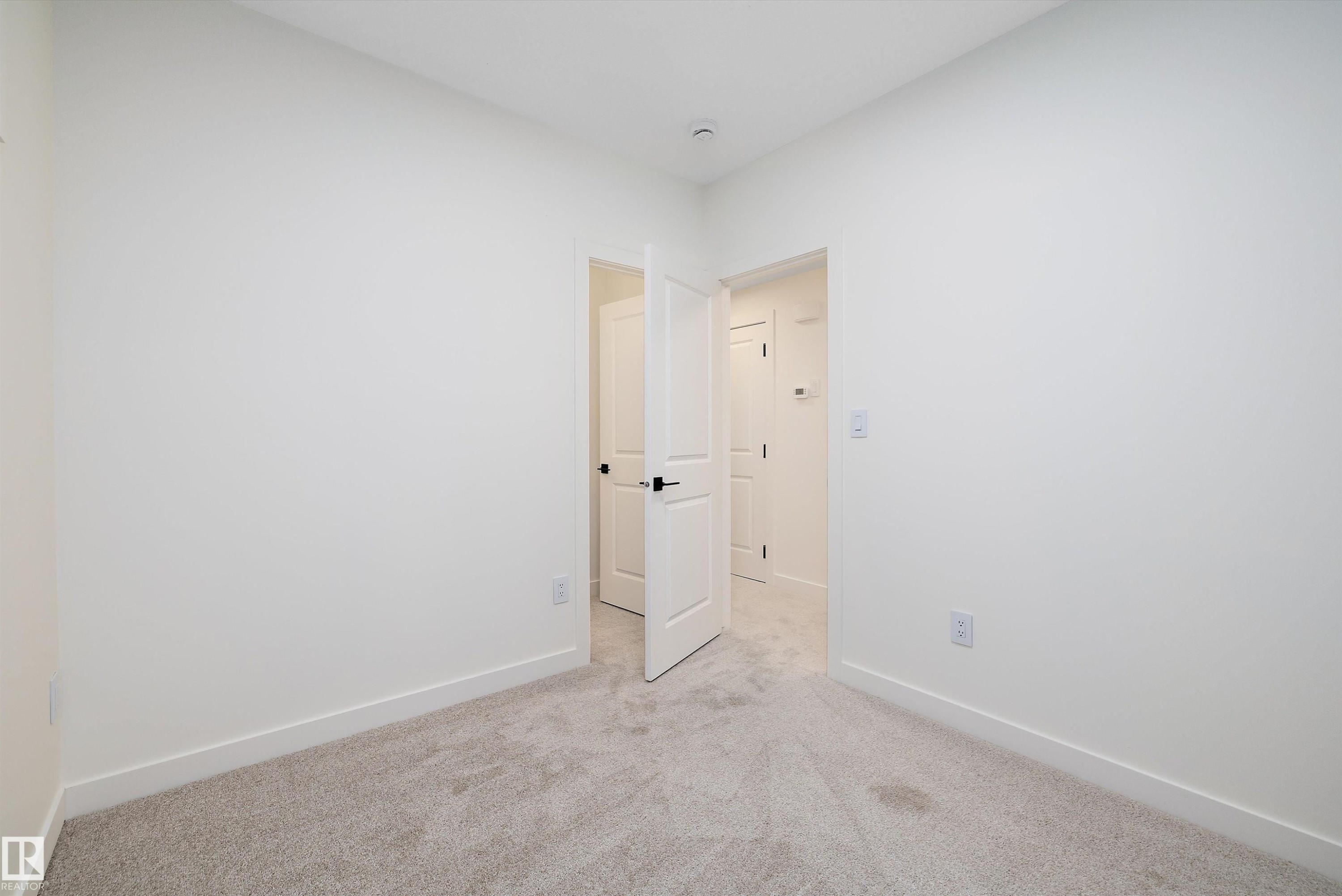 Carpeted room with white walls, white trim, and a white interior door with black hardware - 11418 96 Street, Edmonton, AB - Indoor Photo Showing Other Room