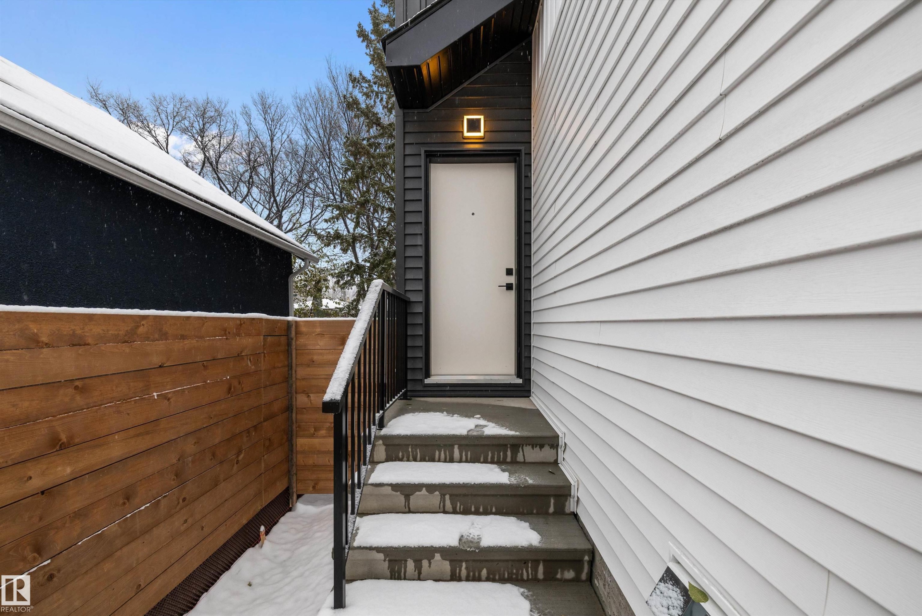 Entryway featuring concrete steps with a black metal handrail, a white door, and a modern exterior light fixture - 11418 96 Street, Edmonton, AB - Outdoor With Exterior