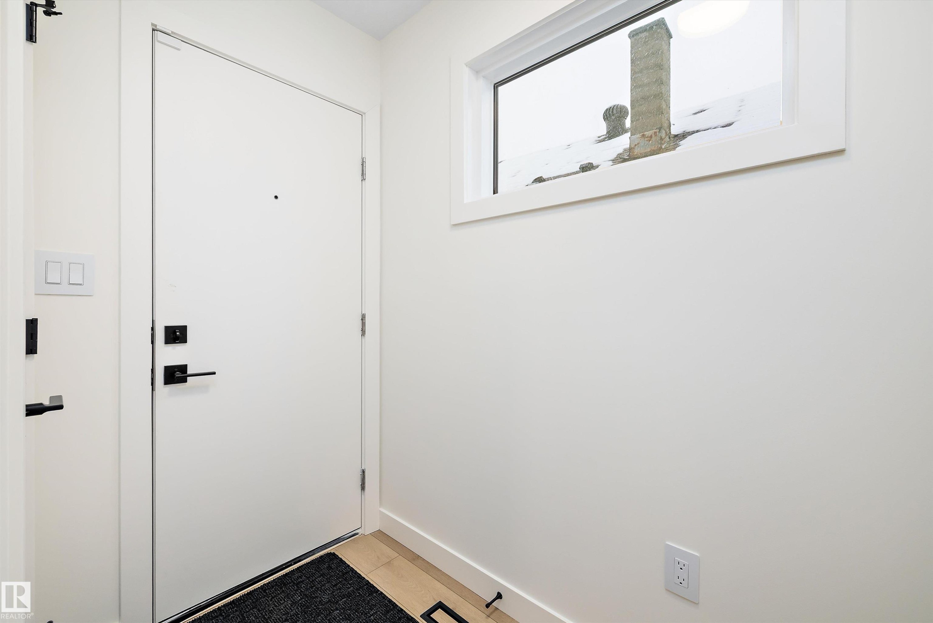 Entryway featuring a solid white door with matte black hardware, transom window, light wood-finish flooring, and white wall finishes - 11418 96 Street, Edmonton, AB - Indoor Photo Showing Other Room