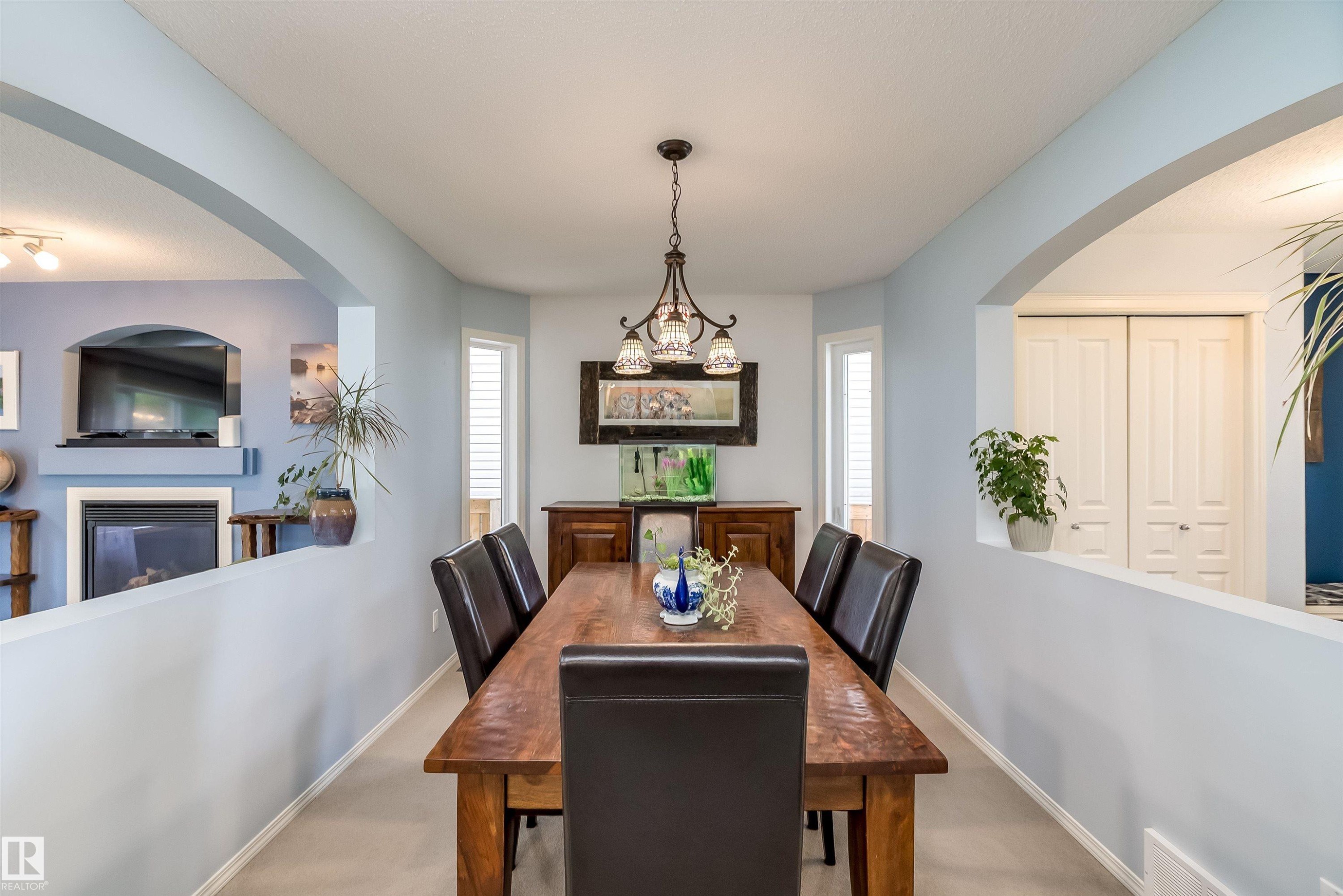 Dining area featuring a central wood-finish table and a decorative chandelier - 59 Rue Monette, Beaumont, AB