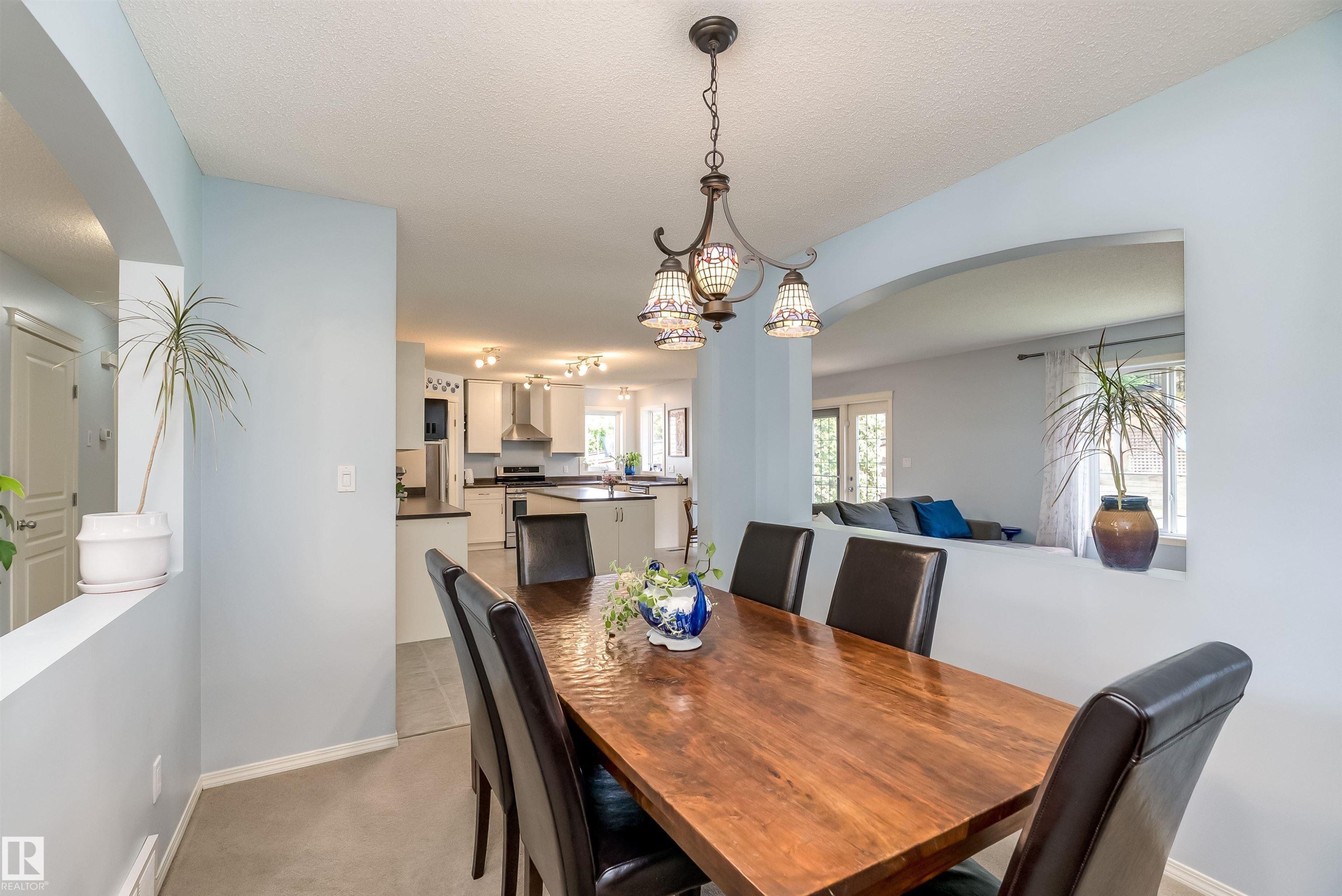 Open-concept kitchen and dining area featuring light-toned cabinetry, a central island with dark countertops, stainless steel appliances, and tile flooring - 59 Rue Monette, Beaumont, AB