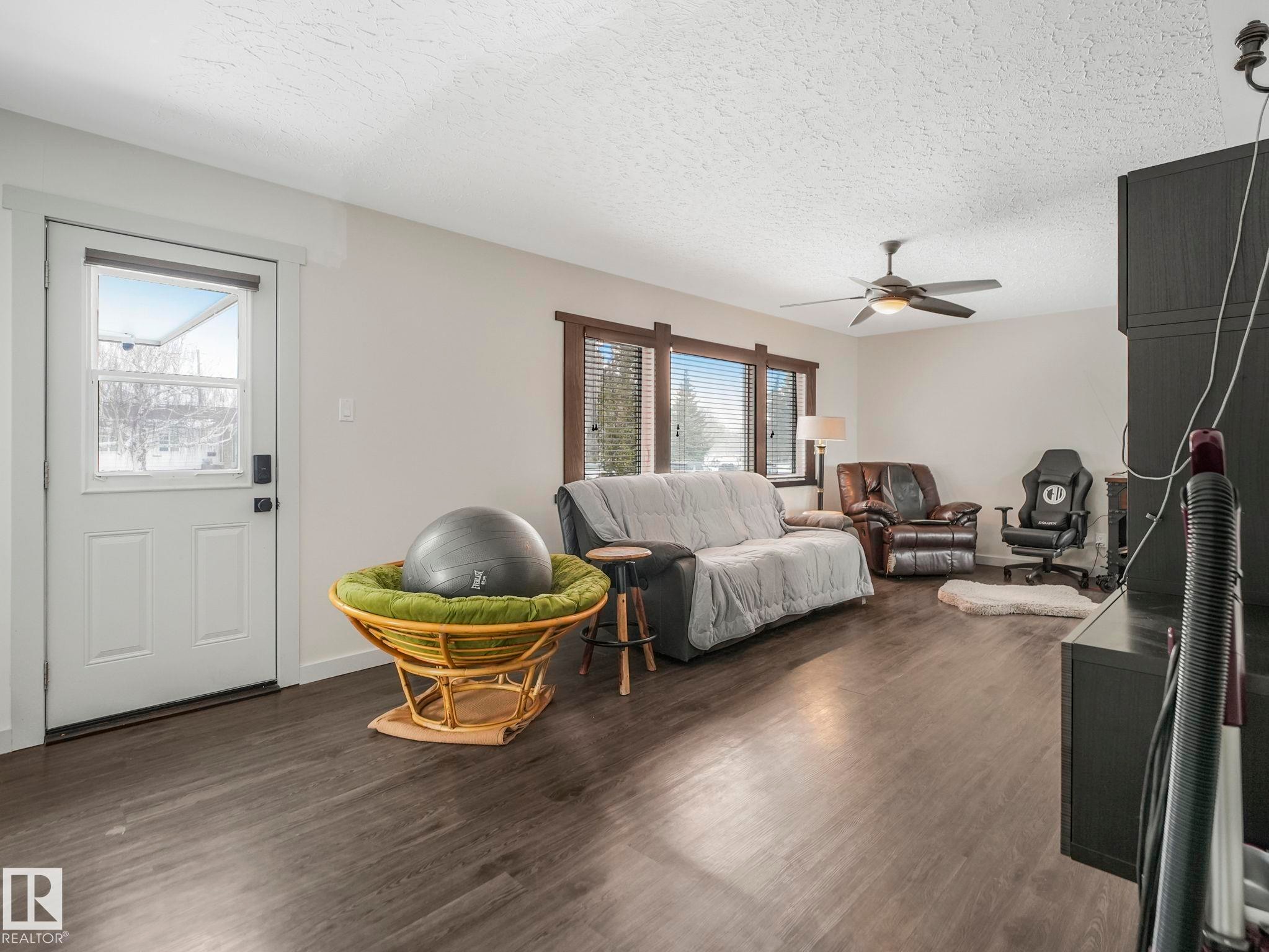 Spacious living area featuring wood-finish flooring, white walls, and a textured white ceiling - 7607 70 Avenue, Edmonton, AB - Indoor