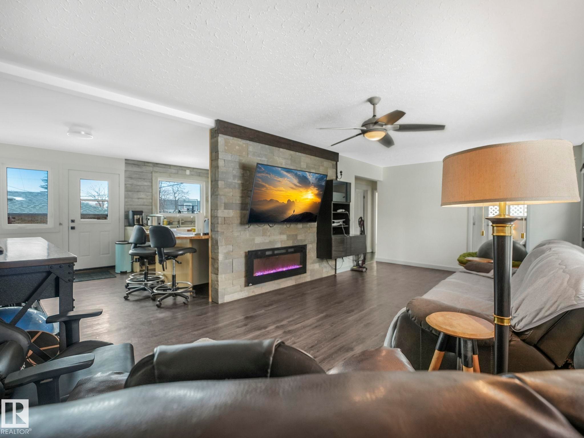 Living space featuring wood-finish flooring and a stone-clad accent wall with an integrated electric fireplace - 7607 70 Avenue, Edmonton, AB - Indoor Photo Showing Living Room With Fireplace