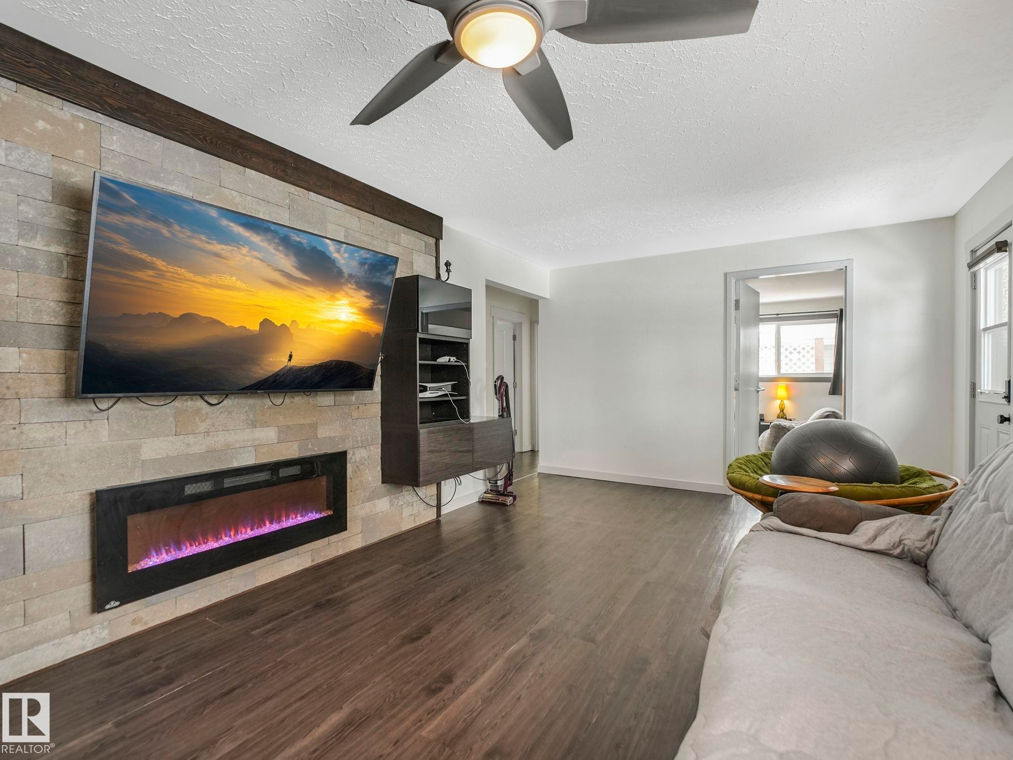Living area featuring a stone accent wall with an integrated electric fireplace - 7607 70 Avenue, Edmonton, AB - Indoor Photo Showing Living Room With Fireplace
