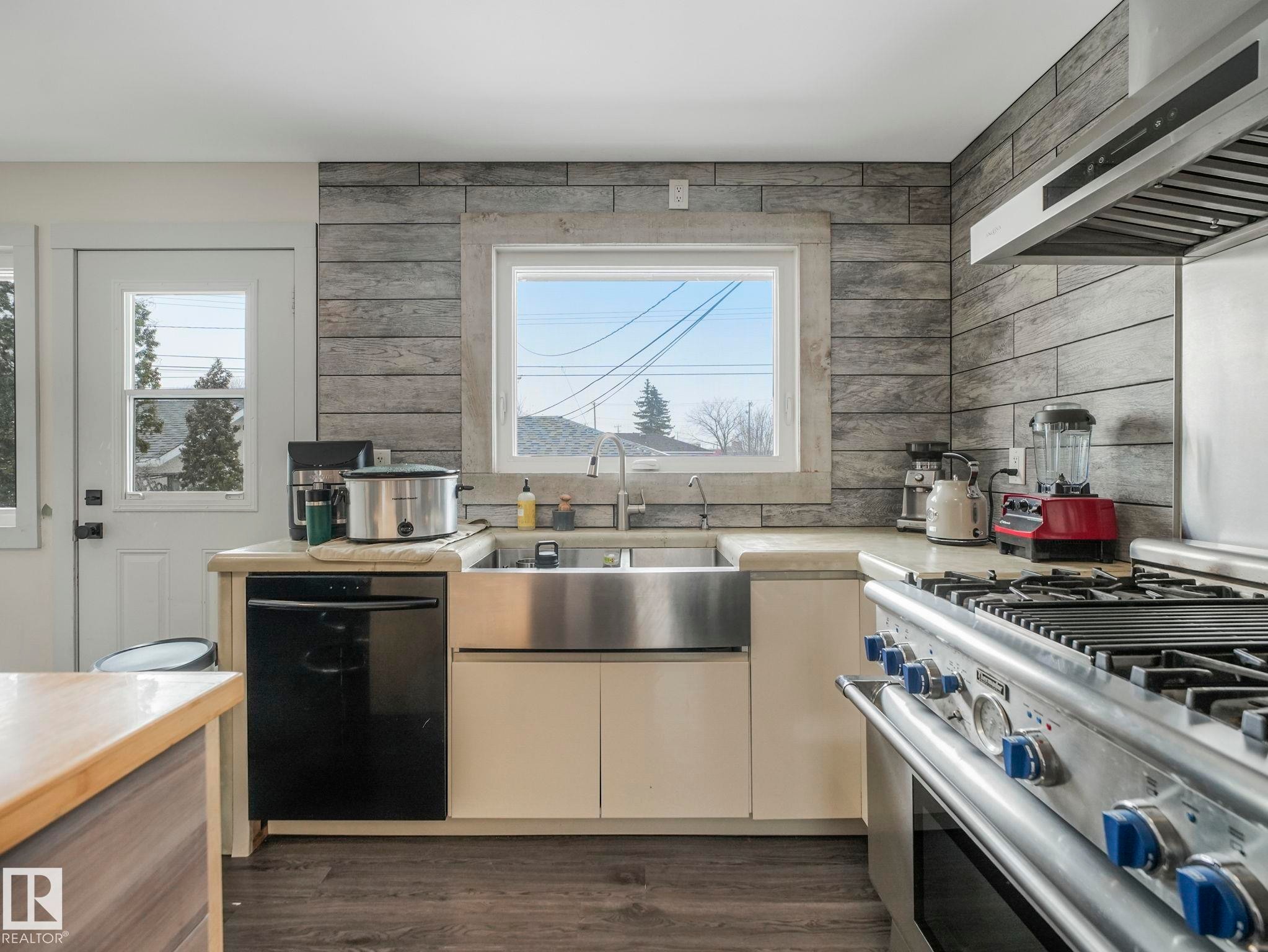 Kitchen featuring a stainless steel farmhouse sink, black dishwasher, and a professional-grade range with a coordinating vent hood - 7607 70 Avenue, Edmonton, AB - Indoor Photo Showing Kitchen With Double Sink