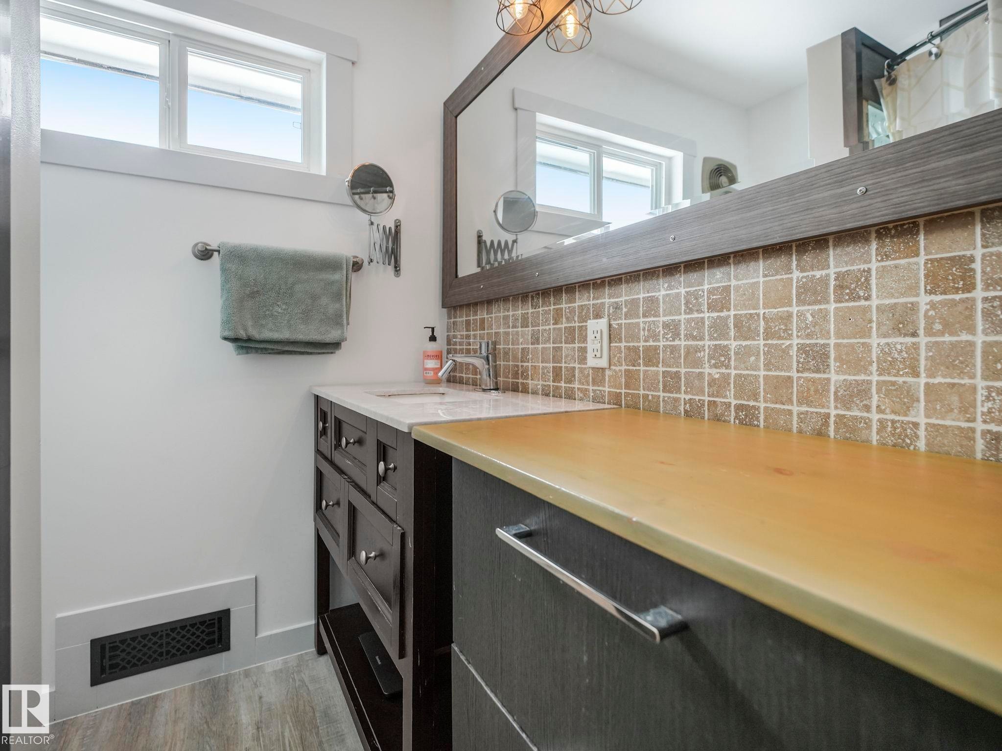 Bathroom featuring a vanity with a white countertop and rectangular sink, complemented by a tiled backsplash - 7607 70 Avenue, Edmonton, AB - Indoor Photo Showing Bathroom