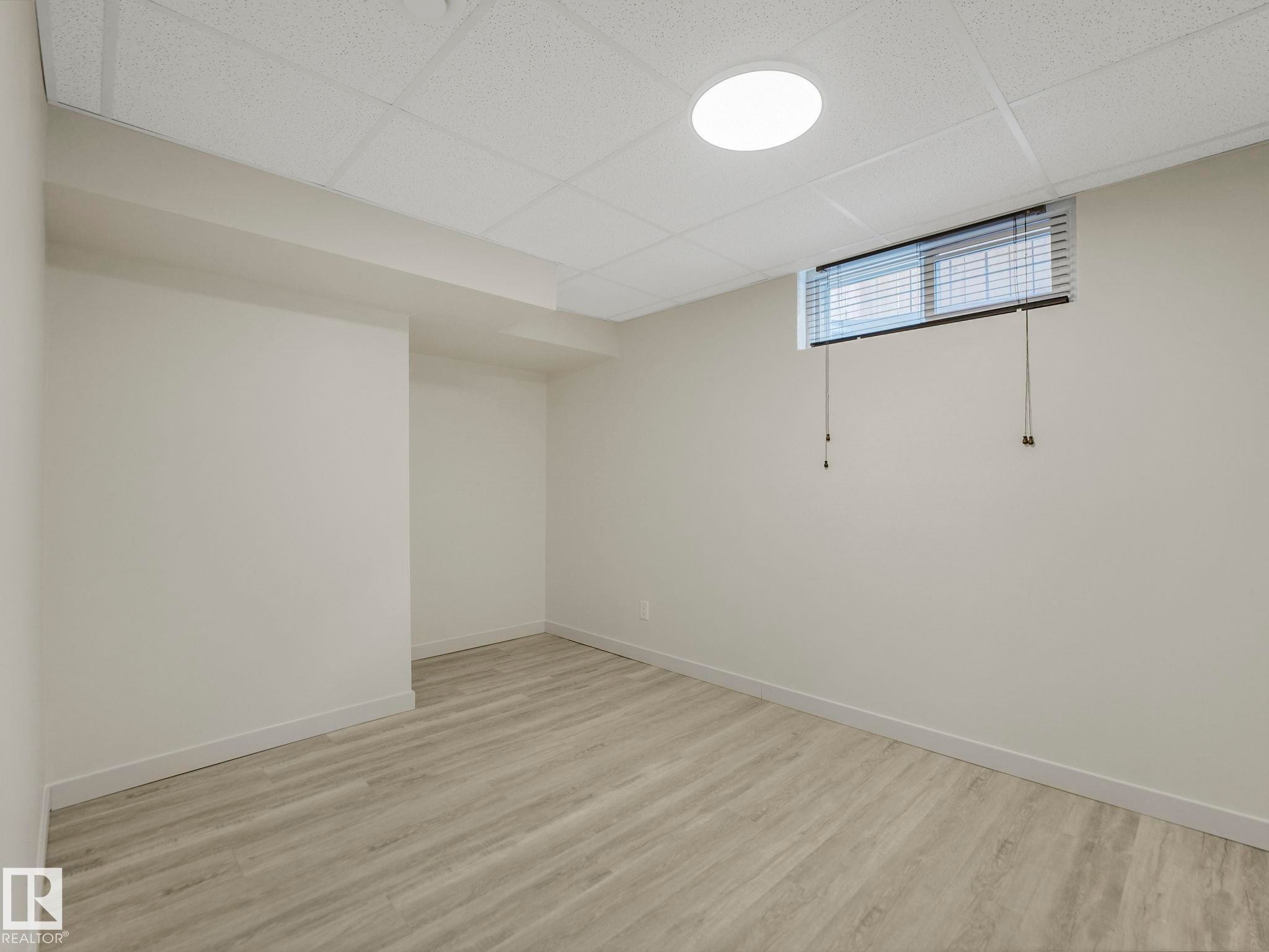 Room with drop ceiling with recessed lighting, and a horizontal window with blinds. Easily converted to a bedroom by resizing window into an egress window. - 7607 70 Avenue, Edmonton, AB - Indoor