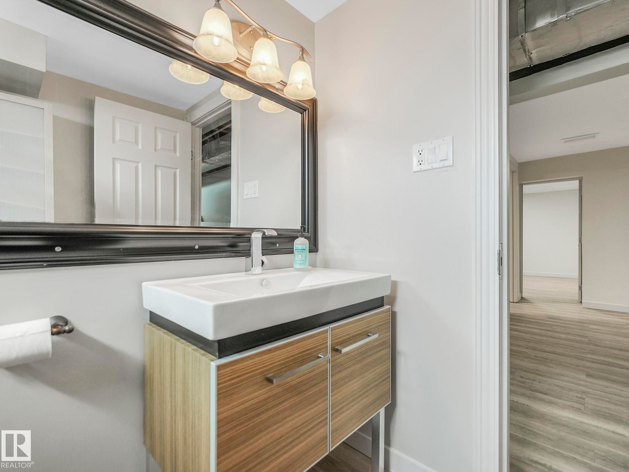 Bathroom vanity featuring a rectangular vessel sink, wall-mounted faucet, and wood-finish cabinetry with silver hardware - 7607 70 Avenue, Edmonton, AB - Indoor Photo Showing Bathroom