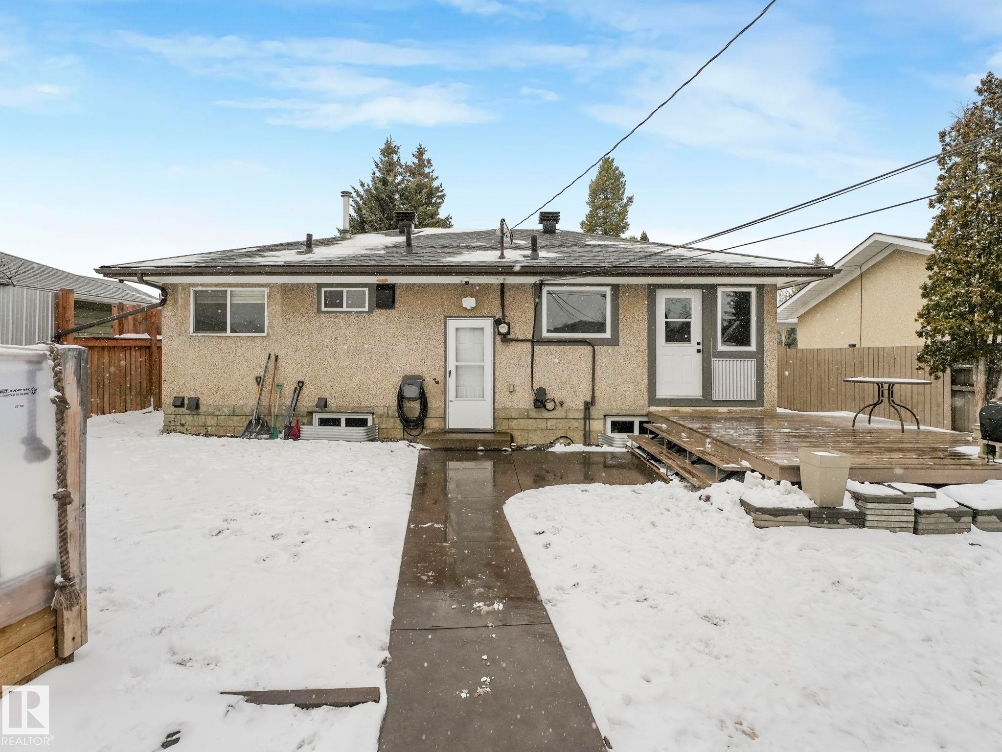Rear exterior featuring stucco siding, multiple windows, a rear entry door, and a multi-level wood-finish deck - 7607 70 Avenue, Edmonton, AB - Outdoor