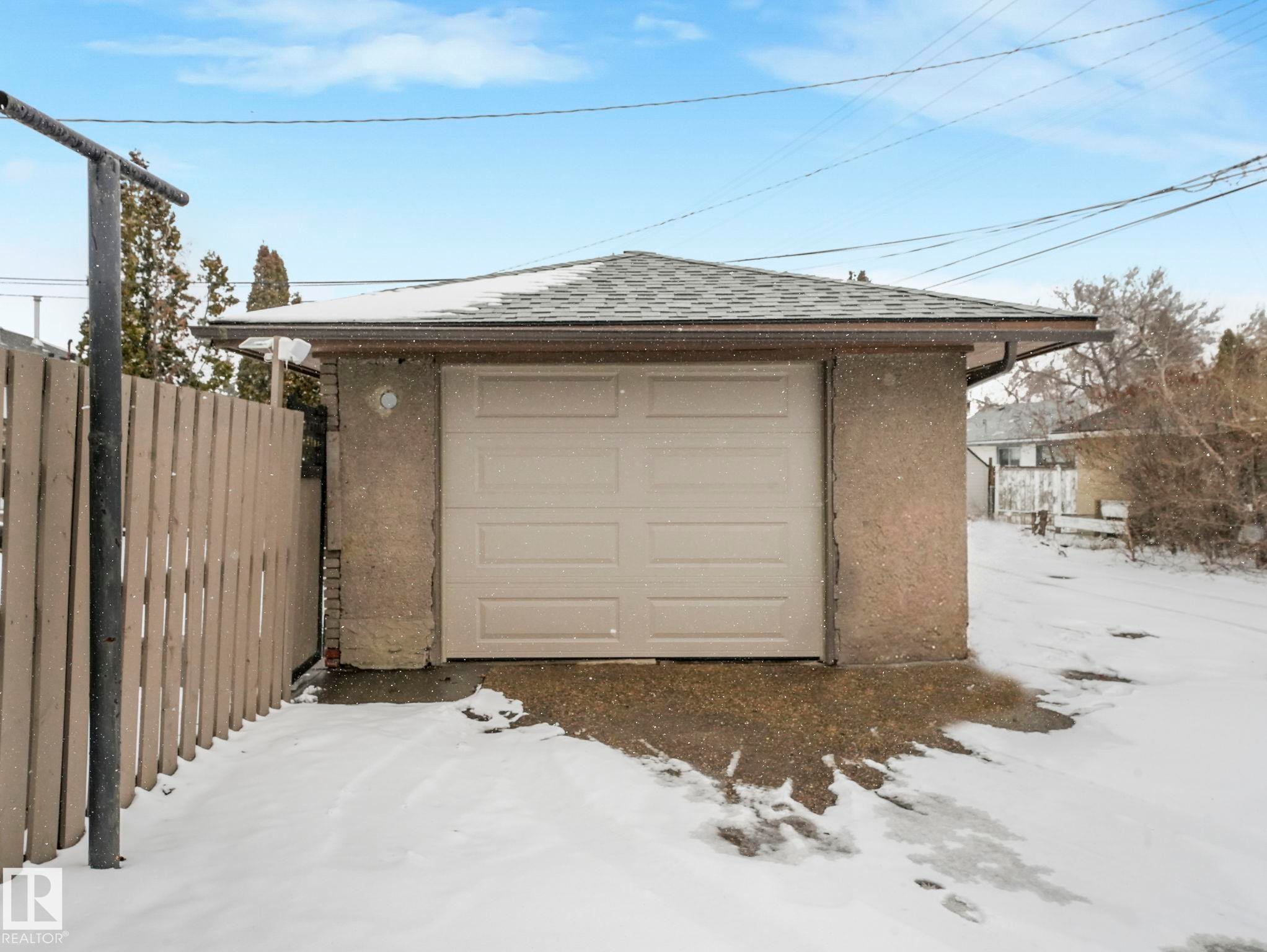 Detached garage with an asphalt shingle roof and a paneled overhead door, complemented by textured exterior walls and a concrete approach - 7607 70 Avenue, Edmonton, AB - Outdoor