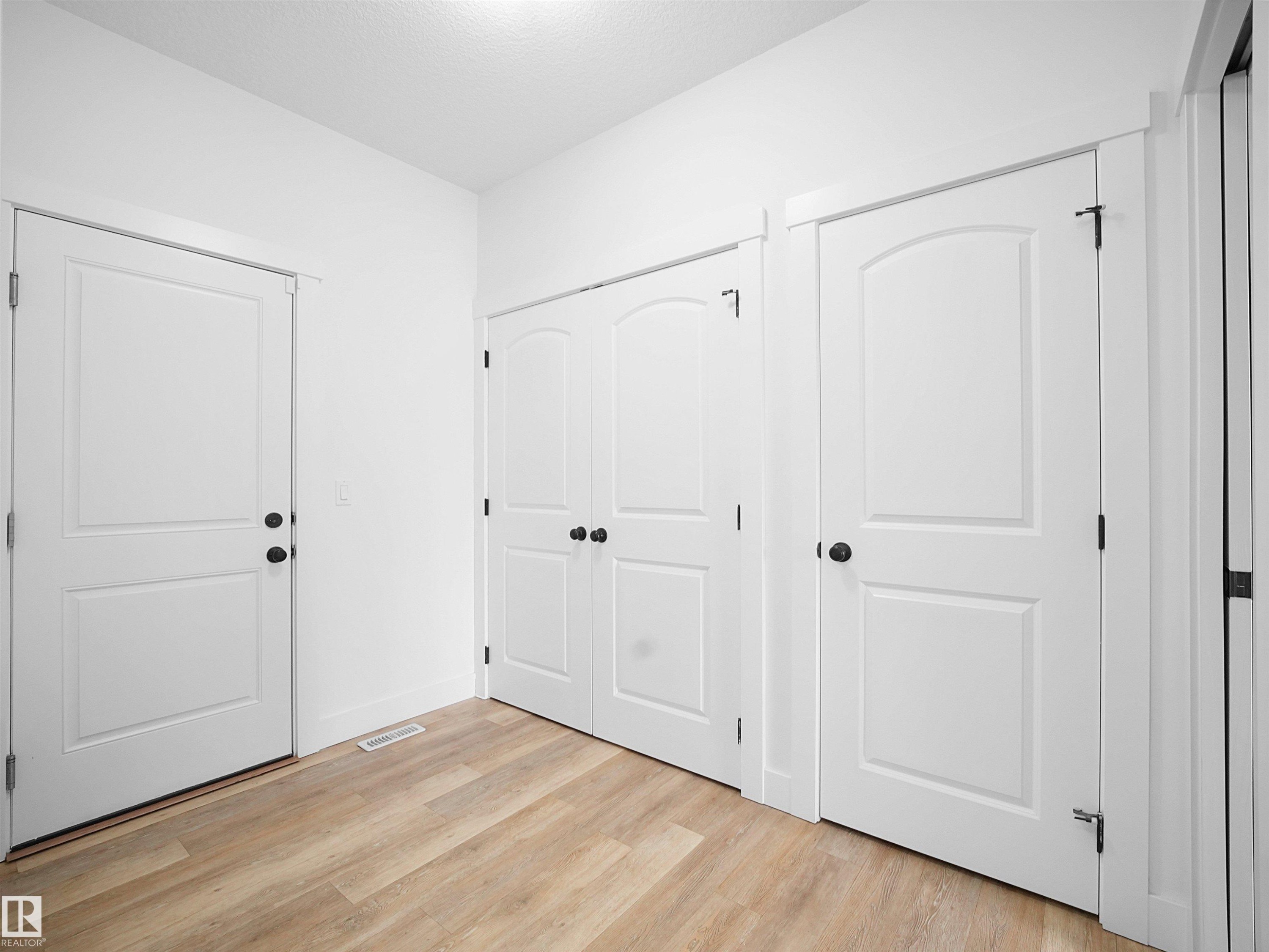Entryway featuring light-toned flooring, white walls, and multiple white paneled doors with dark hardware - 4231 Charles Close, Edmonton, AB - Indoor Photo Showing Other Room