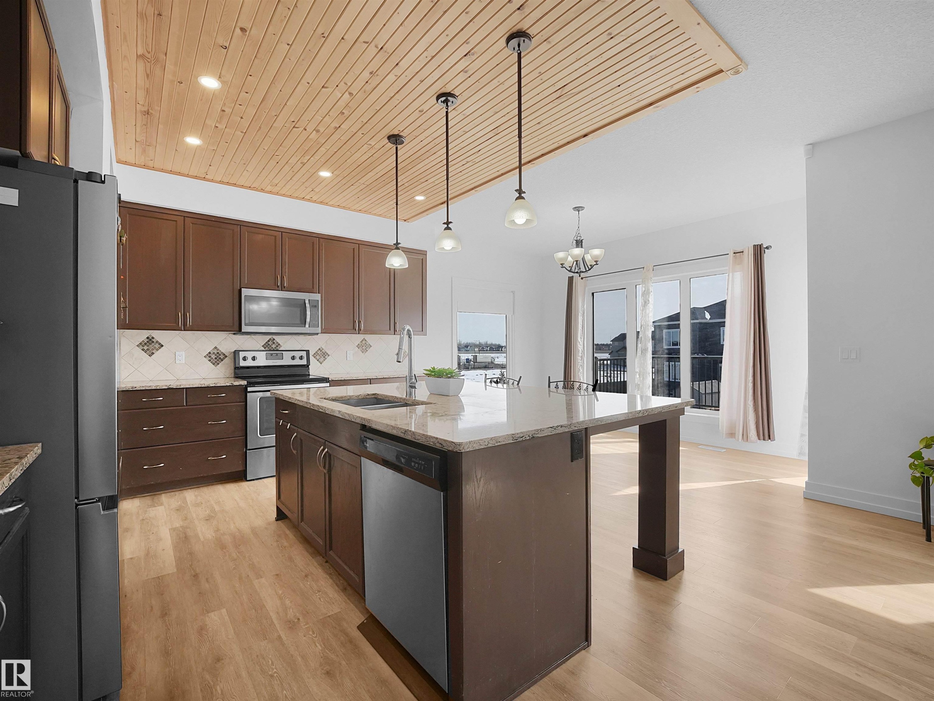 The kitchen features a center island with a sink, stainless steel appliances, dark wood cabinetry, and a tiled backsplash - 4231 Charles Close, Edmonton, AB - Indoor Photo Showing Kitchen With Stainless Steel Kitchen With Upgraded Kitchen