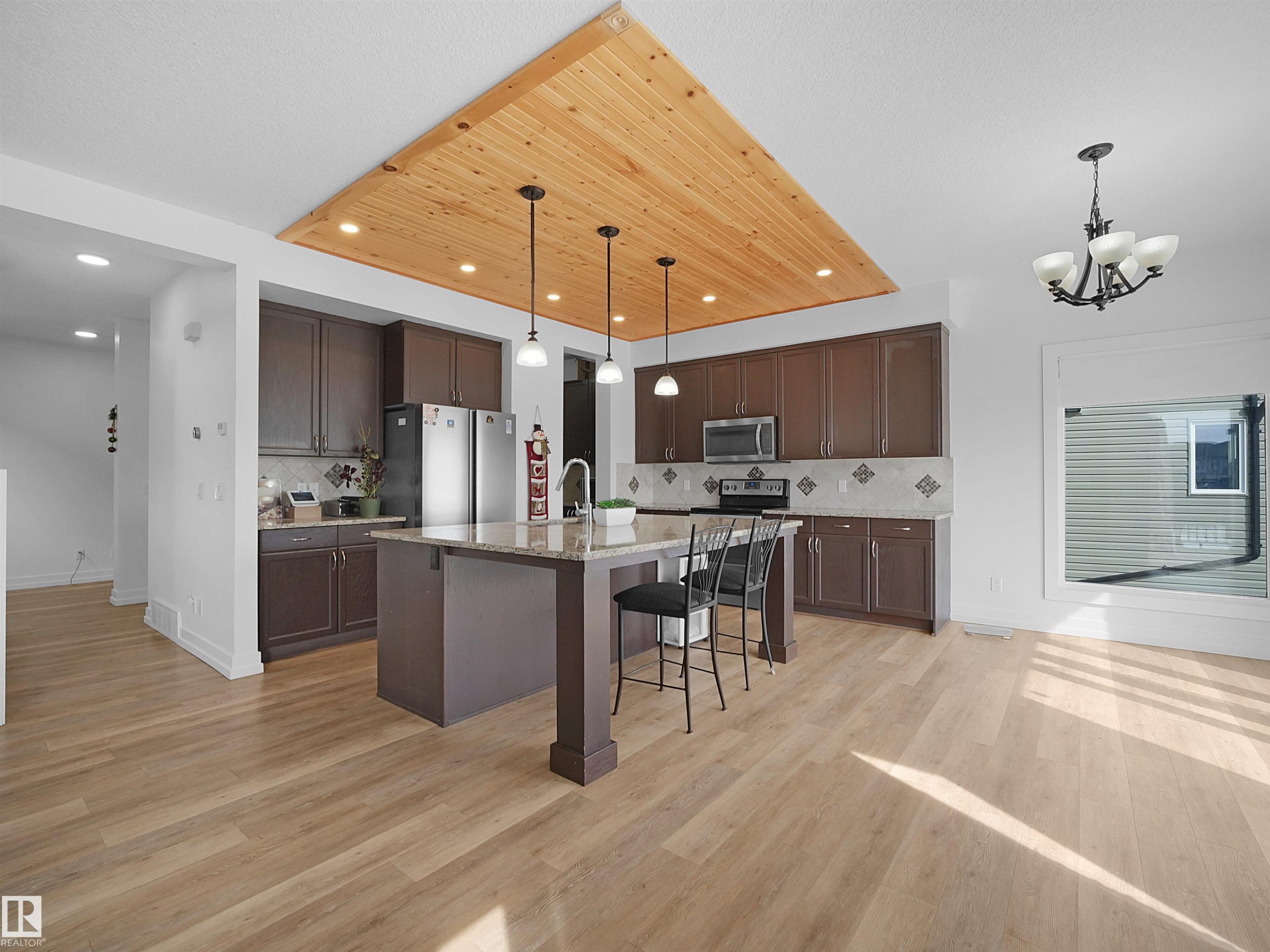 The kitchen features extensive cabinetry, a central island with bar seating, stainless steel appliances, and a tiled backsplash - 4231 Charles Close, Edmonton, AB - Indoor Photo Showing Kitchen With Upgraded Kitchen